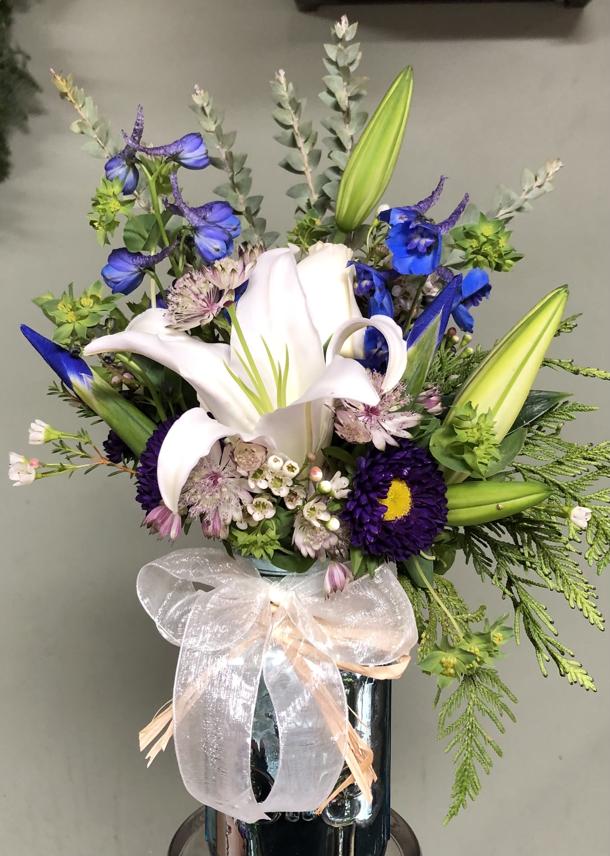 Touch of Blue Touch of Blue - Blue delphinium, Roses, Pines. in vase.