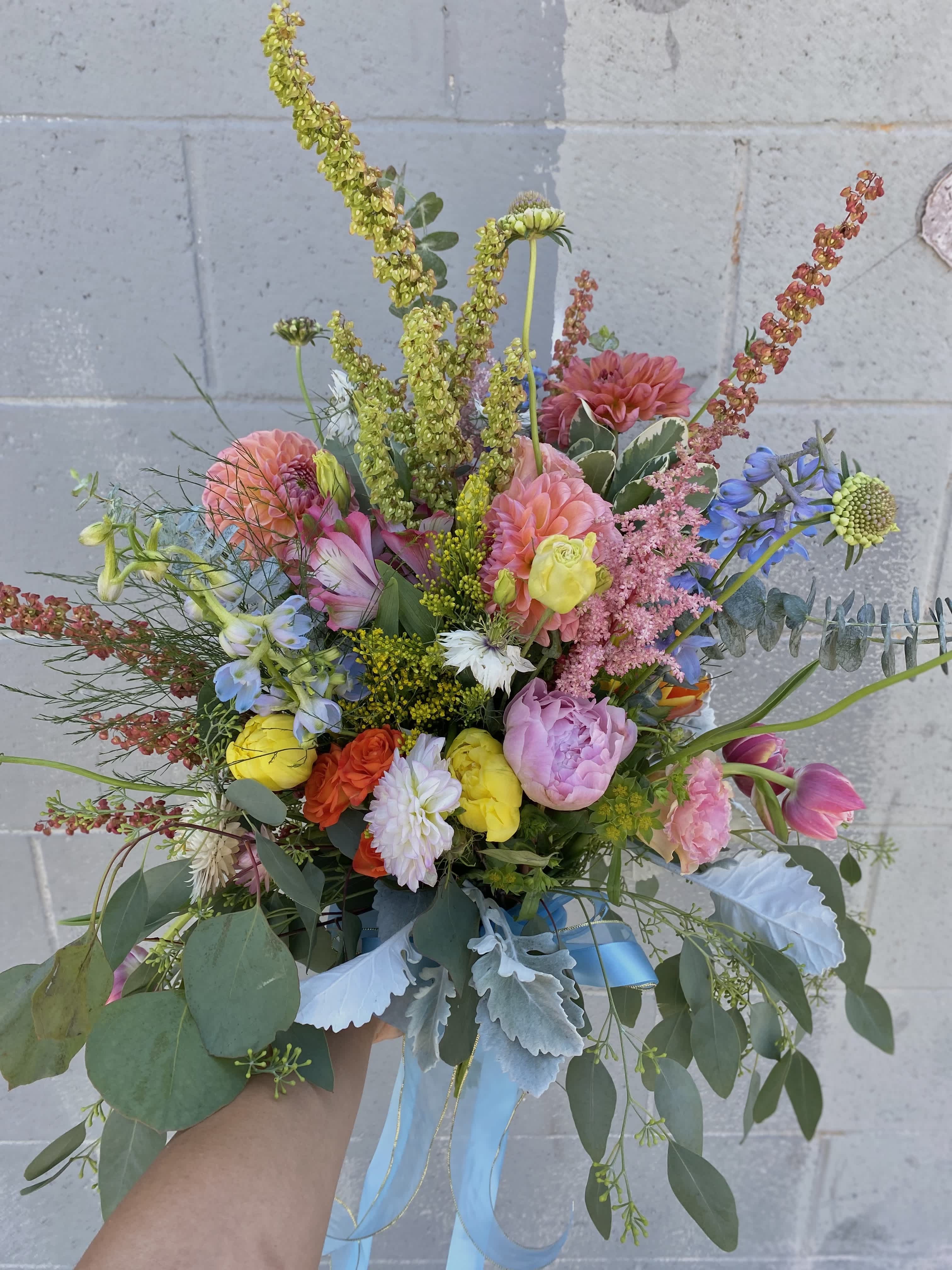 Running Wild  - Make your wedding day unforgettable with this exquisite bridal bouquet. Bursting with a stunning array of peonies, dahlias, tulips, alstroemeria, spray roses, delphinium, and other gorgeous flowers, it's the perfect complement to your special day. 