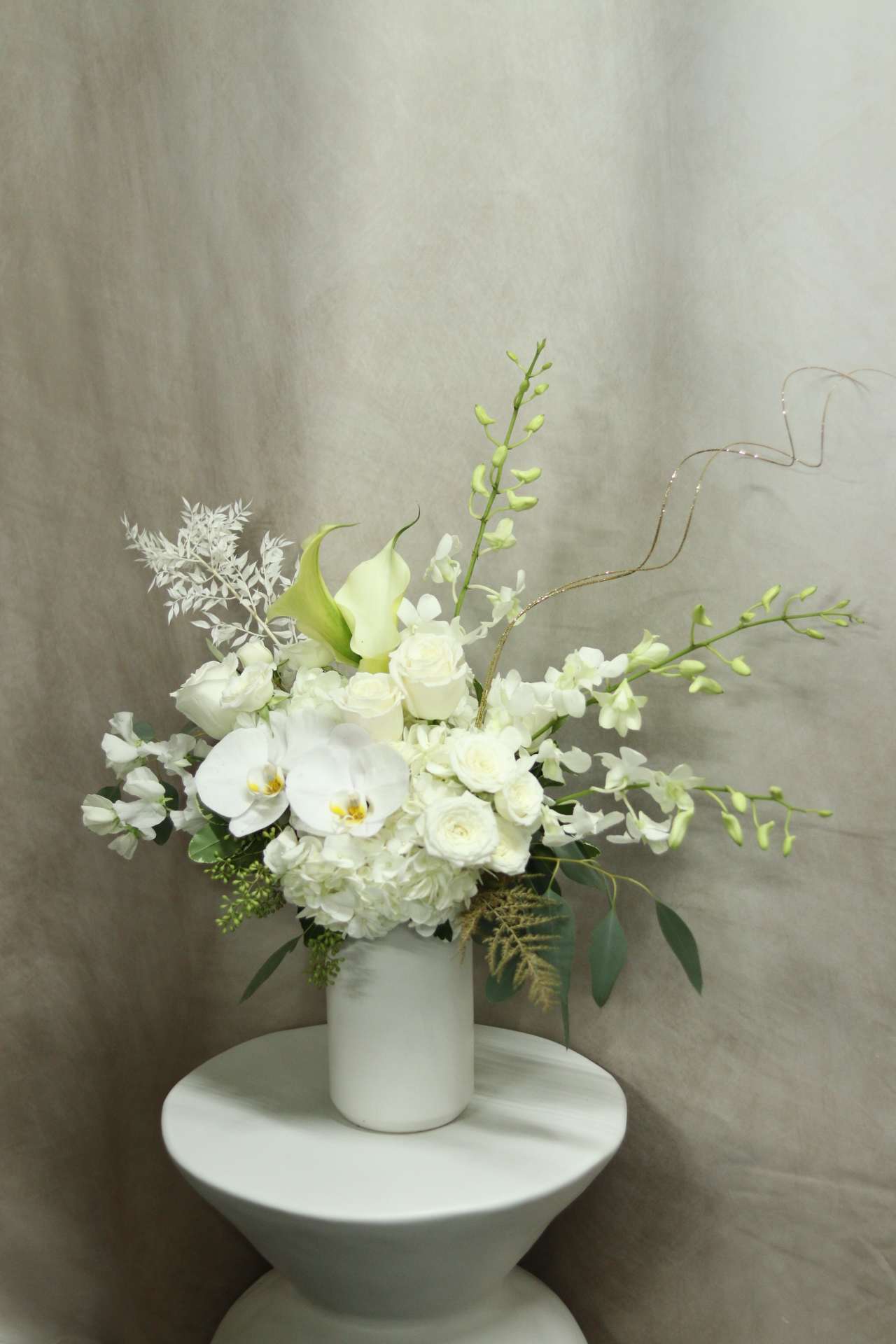 Ethereal Opulence  - Introducing the &quot;Ethereal Opulence&quot; hand crafted by Venetian Flowers - a bouquet, a stunning arrangement that exudes elegance and sophistication. This all white bouquet combines the delicate beauty of roses, calla lilies, dendrobium orchids, sweet peas, and hydrangeas, creating a harmonious blend of textures and shapes. The addition of white orchids and preserved ferns adds a touch of ethereal charm.  The bouquet is meticulously crafted, with each bloom carefully selected for its pristine white hue and impeccable form. The roses add a timeless beauty, while the calla lilies bring a touch of grace and elegance. The dendrobium orchids add an exotic touch, while the sweet peas contribute a soft and romantic element. The hydrangeas provide a lush and voluminous backdrop, adding depth and fullness to the arrangement.  To elevate the bouquet's opulence, delicate touches of gold accents are interspersed throughout. These golden accents add a luxurious shimmer, highlighting the beauty of each bloom and creating a sense of enchantment.  The &quot;Ethereal Opulence&quot; bouquet is the perfect choice for those seeking a sophisticated and chic floral arrangement. Whether it's for a wedding, an anniversary, or a special event, this bouquet will surely leave a lasting impression with its timeless allure and exquisite beauty.