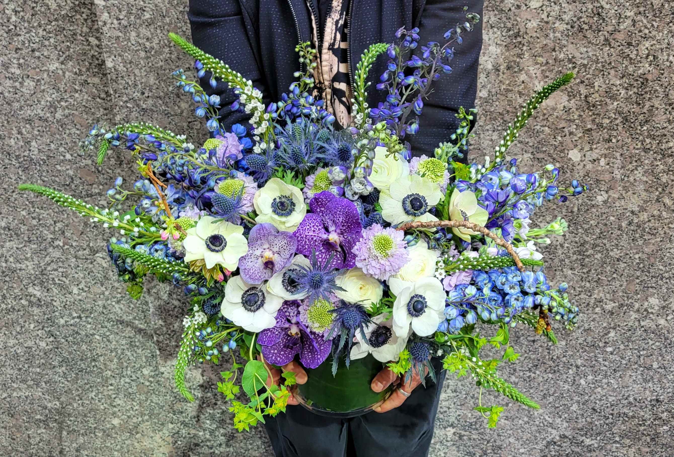 Boca Chica - Immerse yourself in the tranquil beauty of our Boca Chica arrangement, where delicate white anemones sway alongside majestic purple vanda orchids, evoking the serene hues of a seaside paradise. The azure blue delphiniums dance like ocean waves, capturing the essence of coastal bliss. Perfect for bringing a touch of seaside serenity to any space.