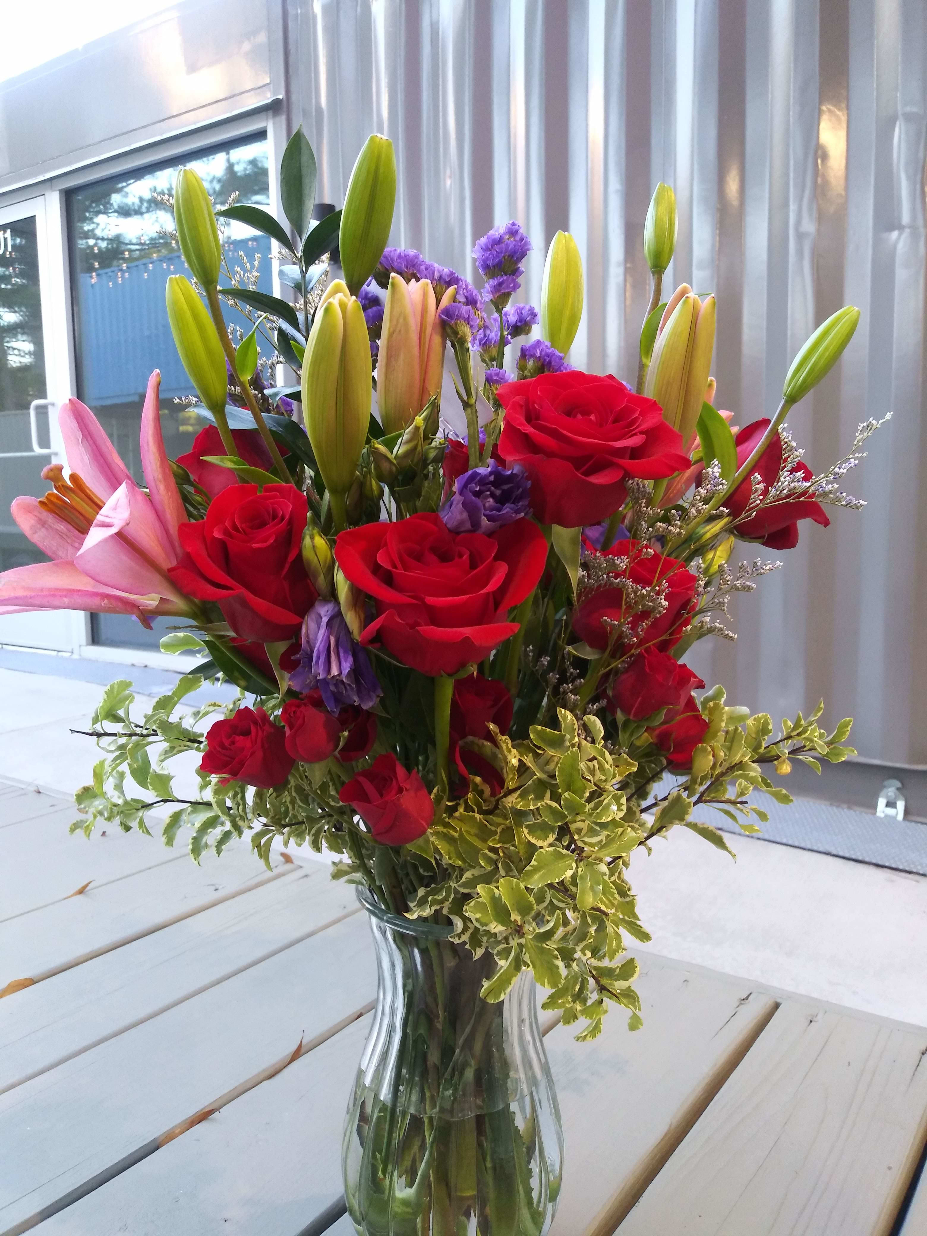 Love in Dis' Club  - A stunning mix of red Roses and red spray roses,pink lilies, purple Lisianthius and statice, assorted filler and variegated greenery in a clear vase. This sultry arrangement will make you start humming that Usher song!
