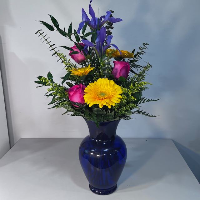 Bright and Blue - This bright Vase arrangement filled with Blue Iris, Yellow Gerbera Daisy and Hot Pink Roses (container or flowers may be substituted due to availability)