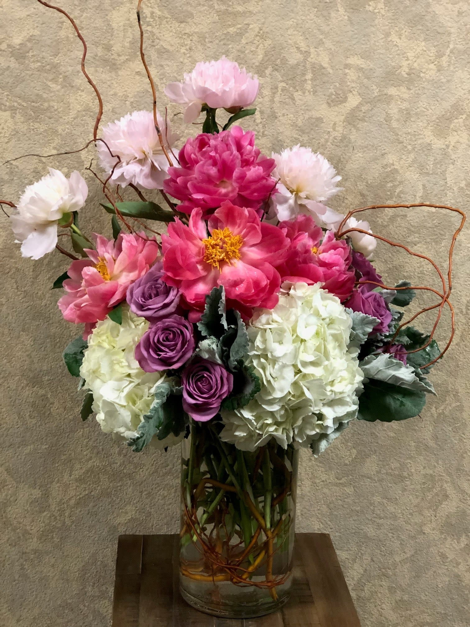 Holland Peonies - Type of Flowers: Pink Peonies, Lavender Roses, White Hydrangeas, and Branches in a large vase. Availability: April, May, and June Substitute Available: Yes Design View: Symmetric Front Facing View Photo shown: Regular