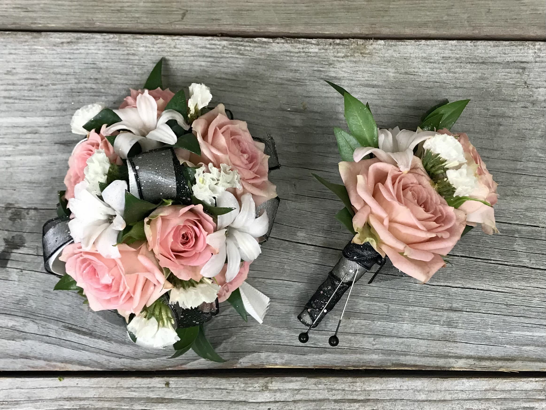 Footloose Corsage Set Footloose Corsage Set - A wrist corsage and boutonniere to coordinate of, pale pink spray roses, white hyacinth, white accent flower with greenery and grey and black sheer sparkle ribbon.