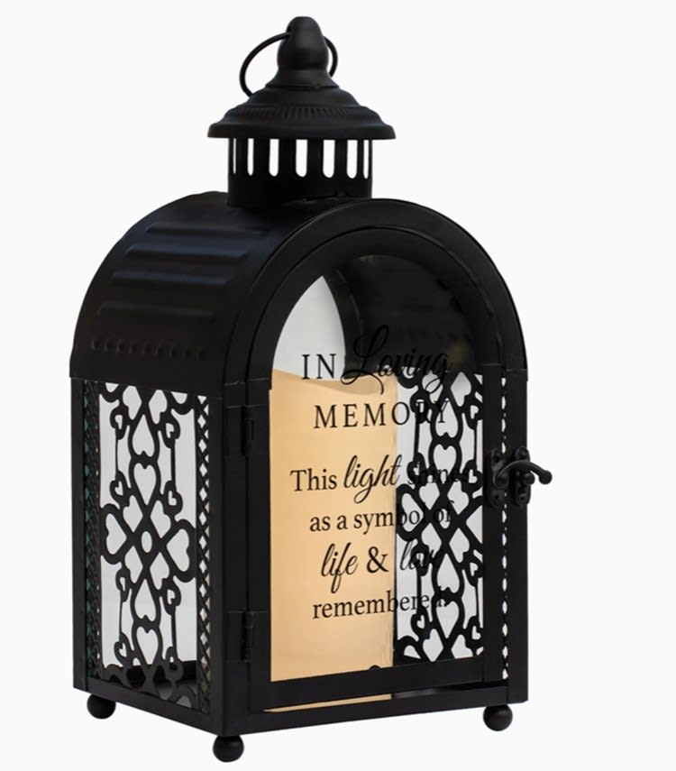 In Loving Memory Lantern - &quot;In loving memory of a life so beautifully lived &amp; a heart so deeply loved.&quot; Displaying a comforting sentiment on front door glass, this exquisite arch shape black metal lantern features lacy open filigree sides, along with large glass window in back and on the front door. Decorative curved latch holds door securely closed. Nicely detailed chimney accent, topped with round carrying handle, is the finishing touch. Lantern is illuminated from within by the soft flickering of a pillar style LED candle, included. Makes a comforting and inspiring presence in times of bereavement. Size of lantern is 11&quot; high; 5.5&quot; wide x 4.5&quot; deep. Candle uses 3 AAA batteries, not included.