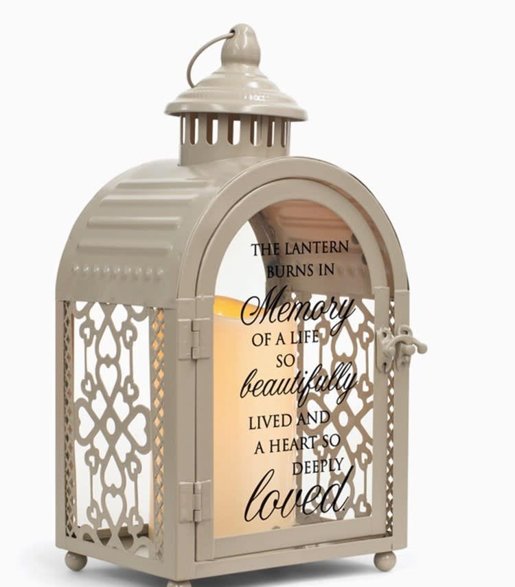 This Lantern Burns in Memory This Lantern Burns in Memory - This lantern burns in memory of a life so beautifully lived and a heart so deeply loved. Exquisite arch shape grey metal lantern features lacy open filigree sides, along with large glass window in back and on the front door. Nicely detailed chimney accent, topped with round carrying handle, is the finishing touch. Glass on door displays a message of comfort, while vintage curved latch holds door securely closed. Lantern is illuminated from within by the soft flickering of a pillar style LED candle, included. Size of lantern is 11" high; 5.5" wide x 4" deep. Candle uses 3 AAA batteries, not included.