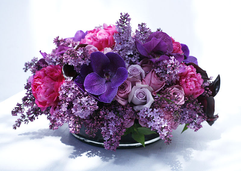 Fairy Pools - Fuschia peonies, lavender roses, purple vanda orchids, lilac, and black calla lilies in a low circular vase. 