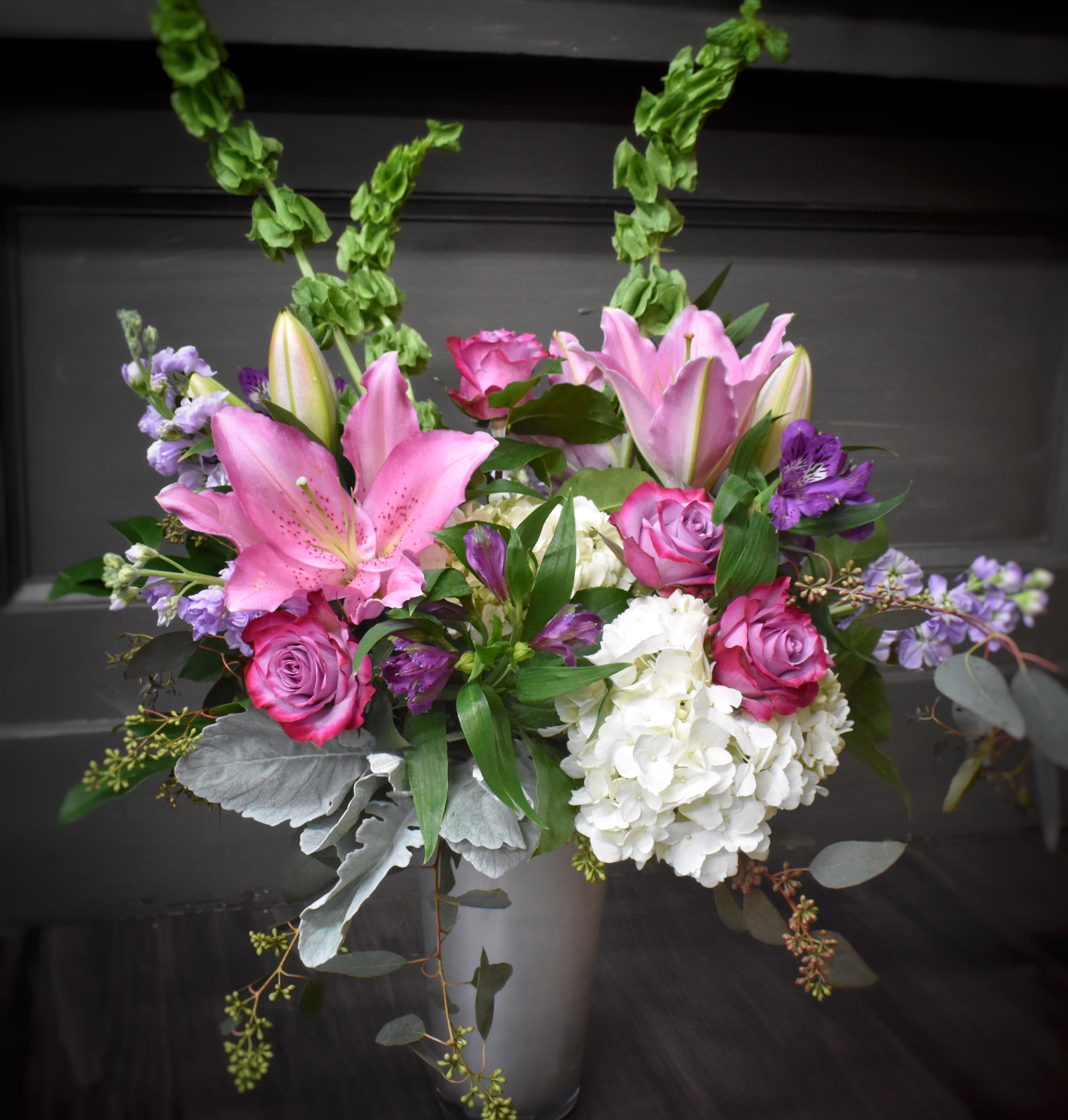 Best Mom In The World - Delivered in an elegant silver tone colored glass vase, is a grouping of beautiful flowers in shades of purple, lavender and pink.  Always a favorite color palette.