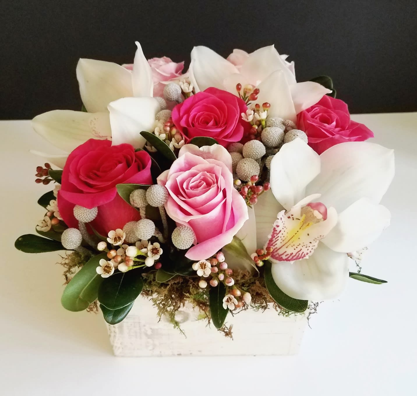 Sweet Innocence - This modern style garden box is filled with hot pink and light pink roses, white cymbidium orchids, wax flower and silvery berzelia balls.