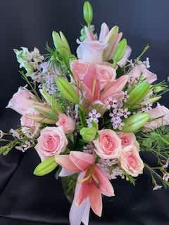To Mother With Love - In a clear glass vase, A beautiful Pink Lily is surrounded by pink roses &amp; pink wax flowers accompanied by a pink bow.