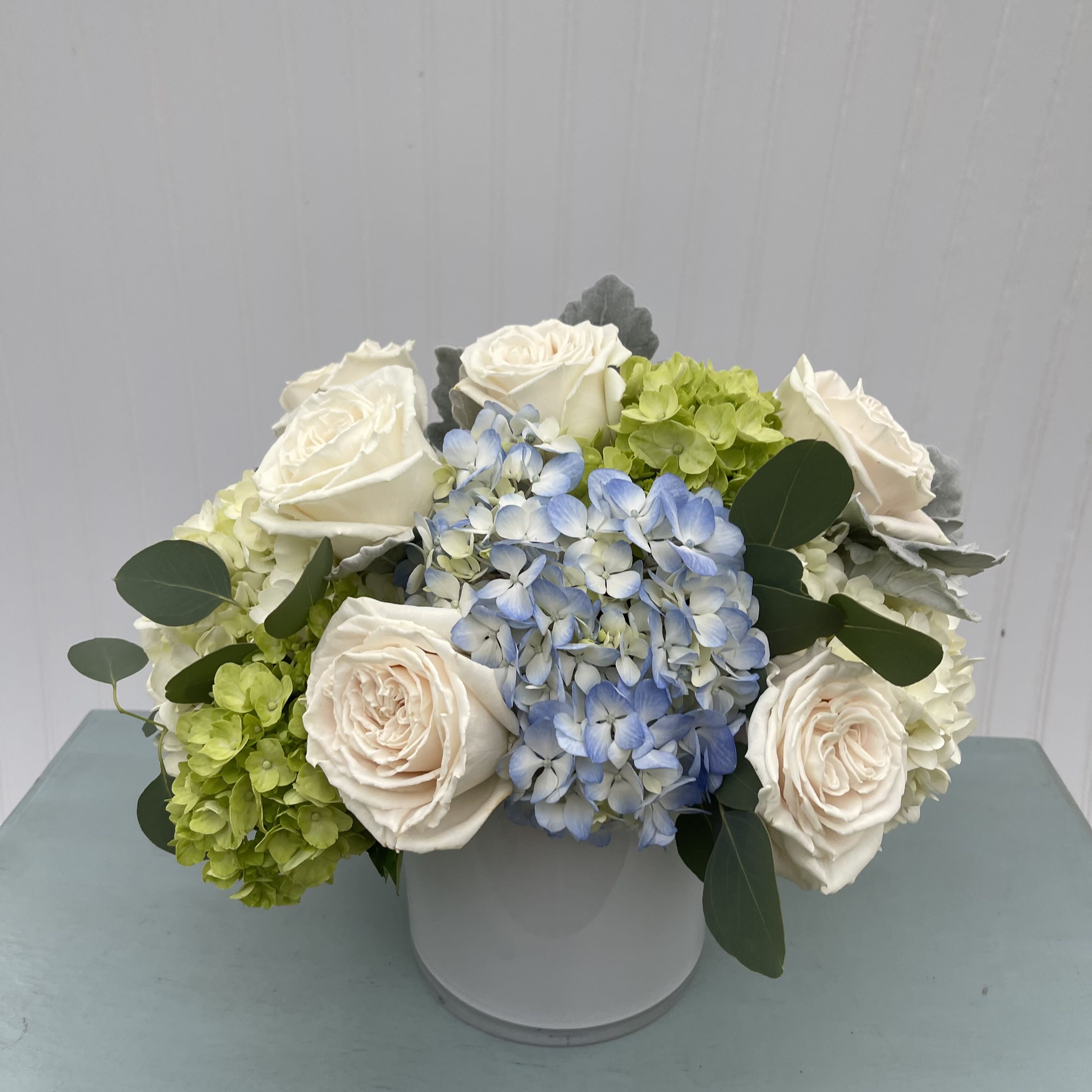 Light + Love  - Soothing blue, green and white hydrangea and roses arranged in a low white glass vase. 