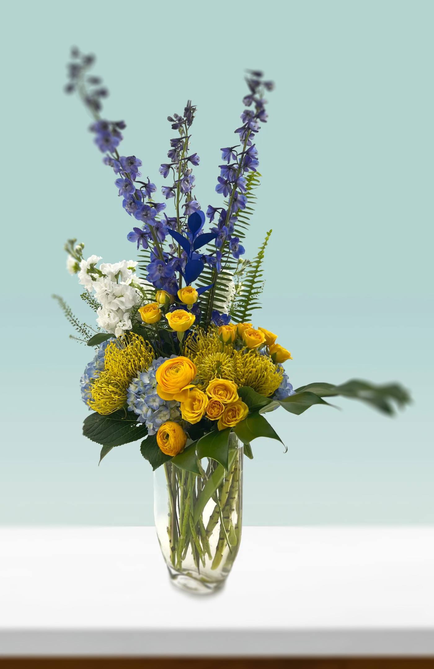 Limitless Joy - Boundless joy to be found with this bold combination of yellows and blues. Flowers include protea, spray roses, hydrangea, and delphinium.