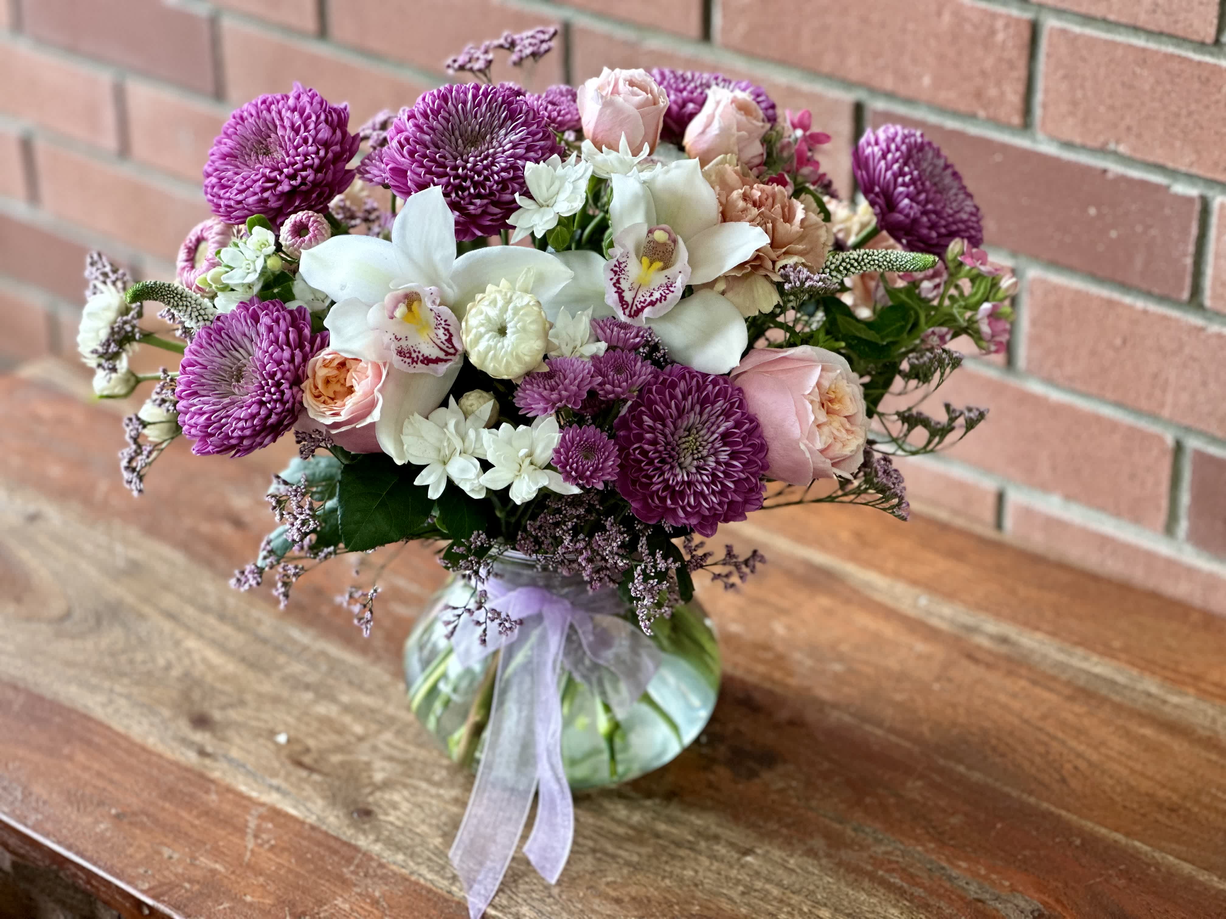Lavender Love Bouquet  - Send a gorgeous arrangement with peach garden roses, lavender mums, white orchids, peach spray garden roses, button mums, filler flowers and more in a clear vase accented with ribbons. 