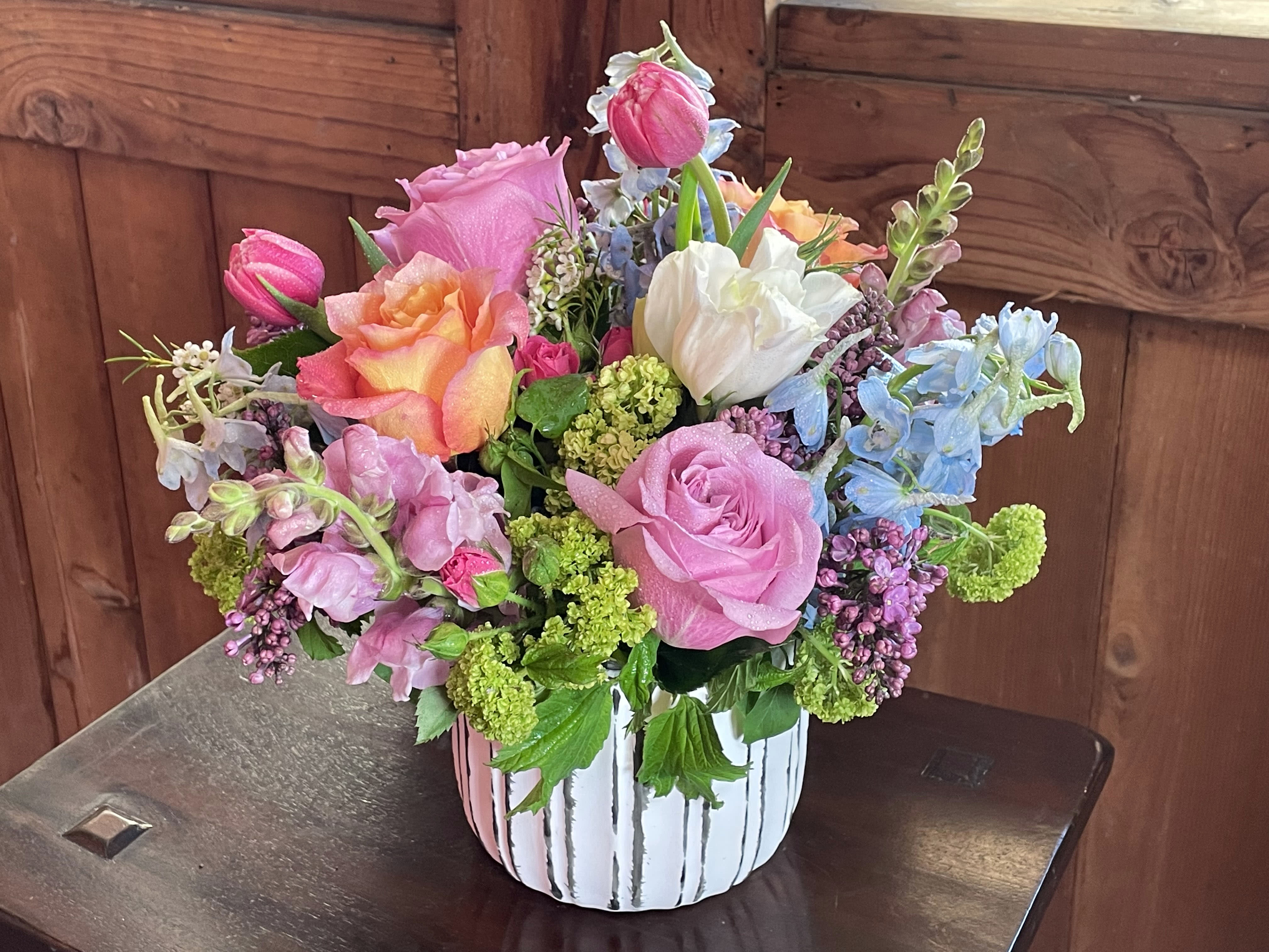 Painted Lady - A dashing and vibrant mix of all our seasonal Spring favorites!  Featuring a fragrant mix of lilac, viburnum, roses, tulips, delphinium, snapdragons, and seasonal filler and greens in a ceramic stripe pot.  Approximately 10&quot;x8&quot;