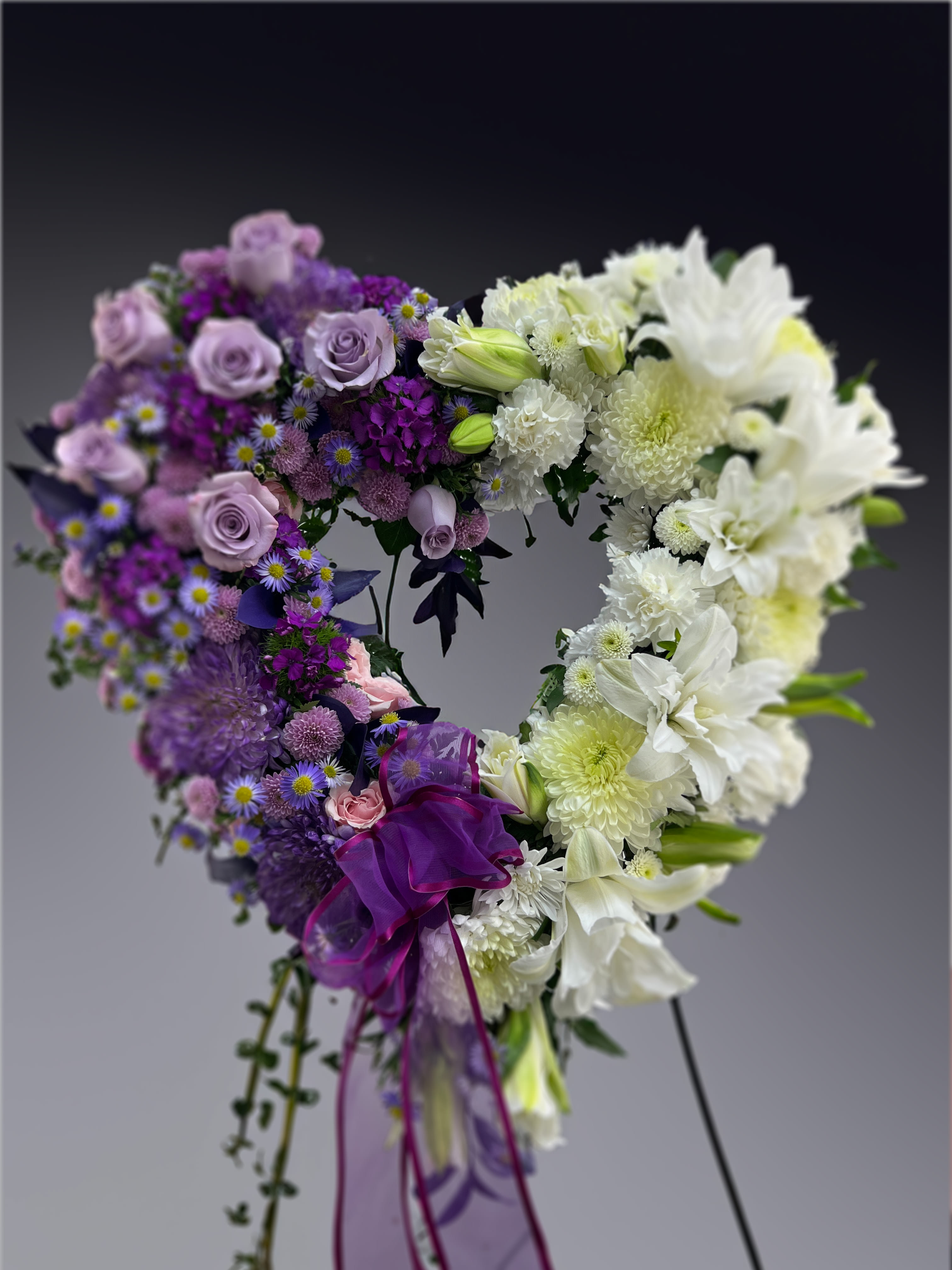 Loving Memory Heart  - When words aren't enough to express your sympathy and love, this open heart spray of purples and whites conveys your condolences thoughtfully. It is crafted of beautiful purple roses and white mums.  Colors and assortment may vary. The heart measures approximately 20” H x 20&quot;L without easel.