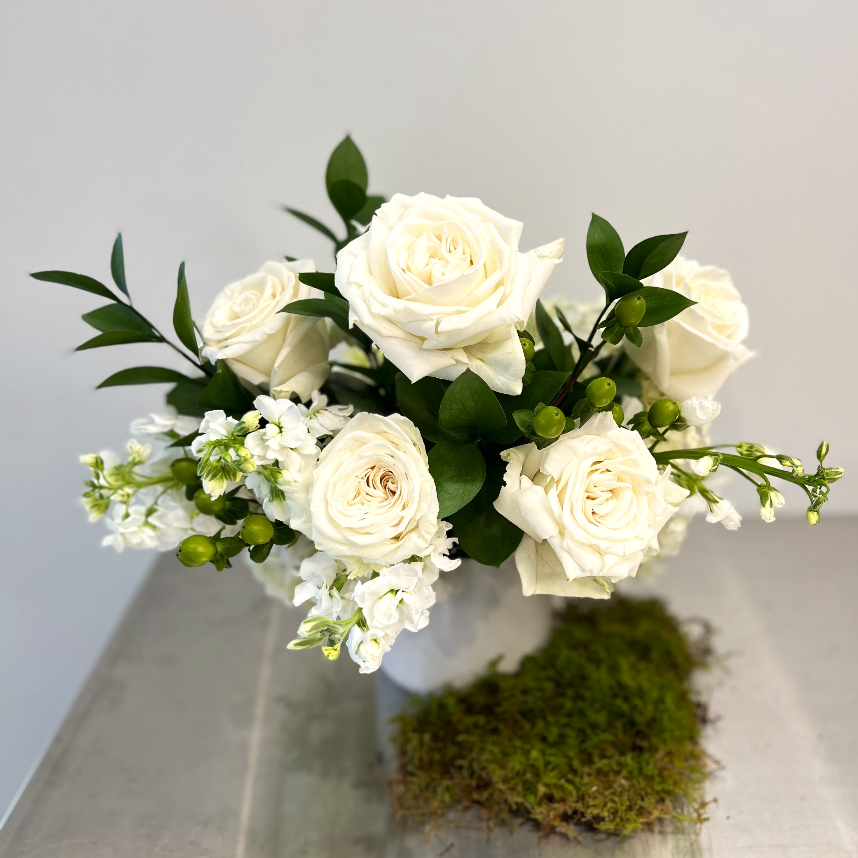Bright White - Crisp and Clean - Perfect for a gift when you're not sure what else to do!  From the coffee table, to the kitchen island - this arrangement is one our favorites for sure.  White Hydrangea, White Garden Roses, fragrant Stock, Hypericum Berries, and assorted greenery.  Ranging in size from 10&quot; to 18&quot; based on price point.  Arranged in a white ceramic container.