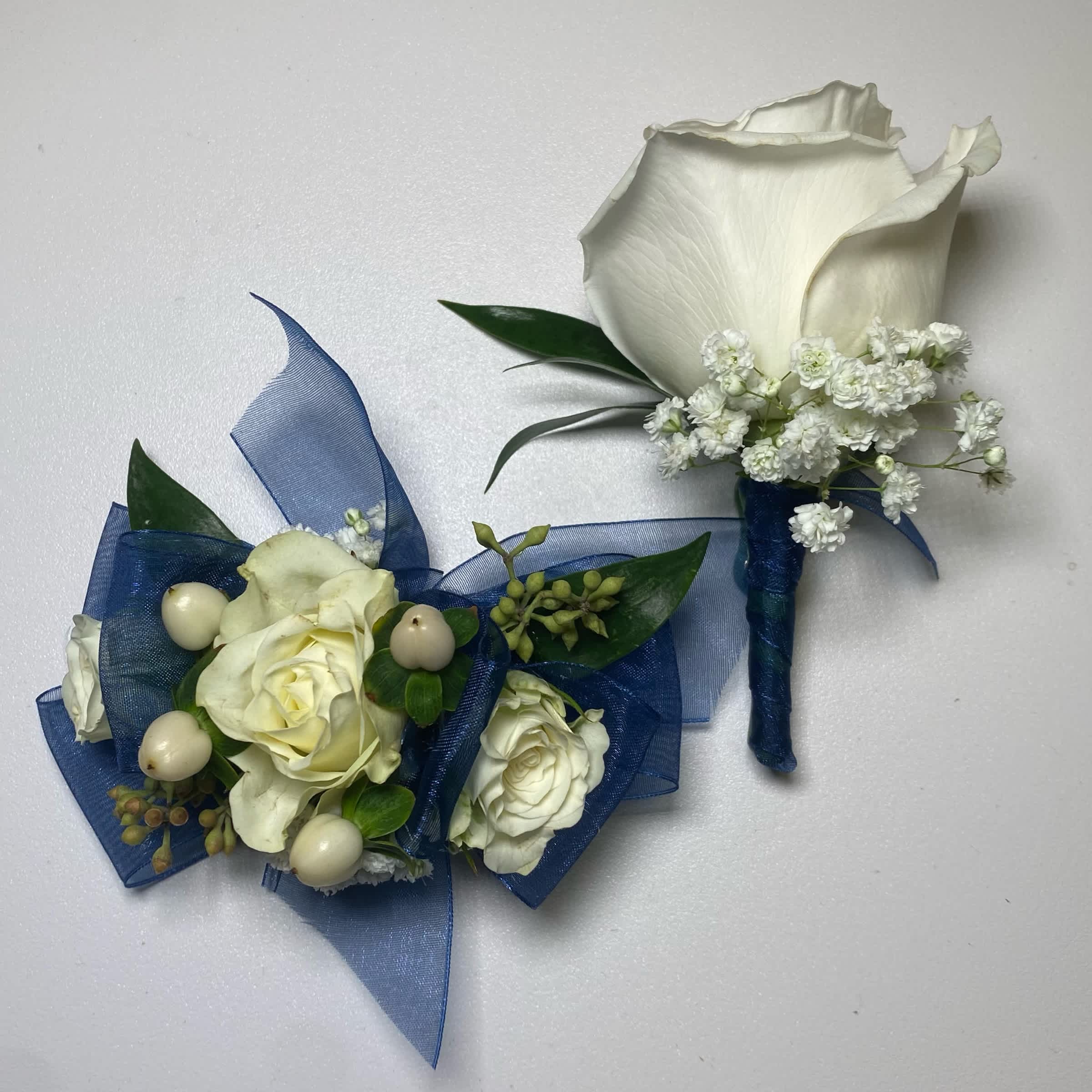 Navy Blue Set - Prom/ Wedding - This White Rose Corsage and Boutonniere Includes an Adult Size Elastic Wristband Corsage and Magnetic Boutonniere with Navy Blue Chiffon Ribbon. The Corsage Includes White Spray Roses, Hypericum Berries, Gentle Greenery and Seeded Eucalyptus. The Boutonniere includes a White Rose with Babies Breath and Gentle Greenery. Or as Similar as Possible.