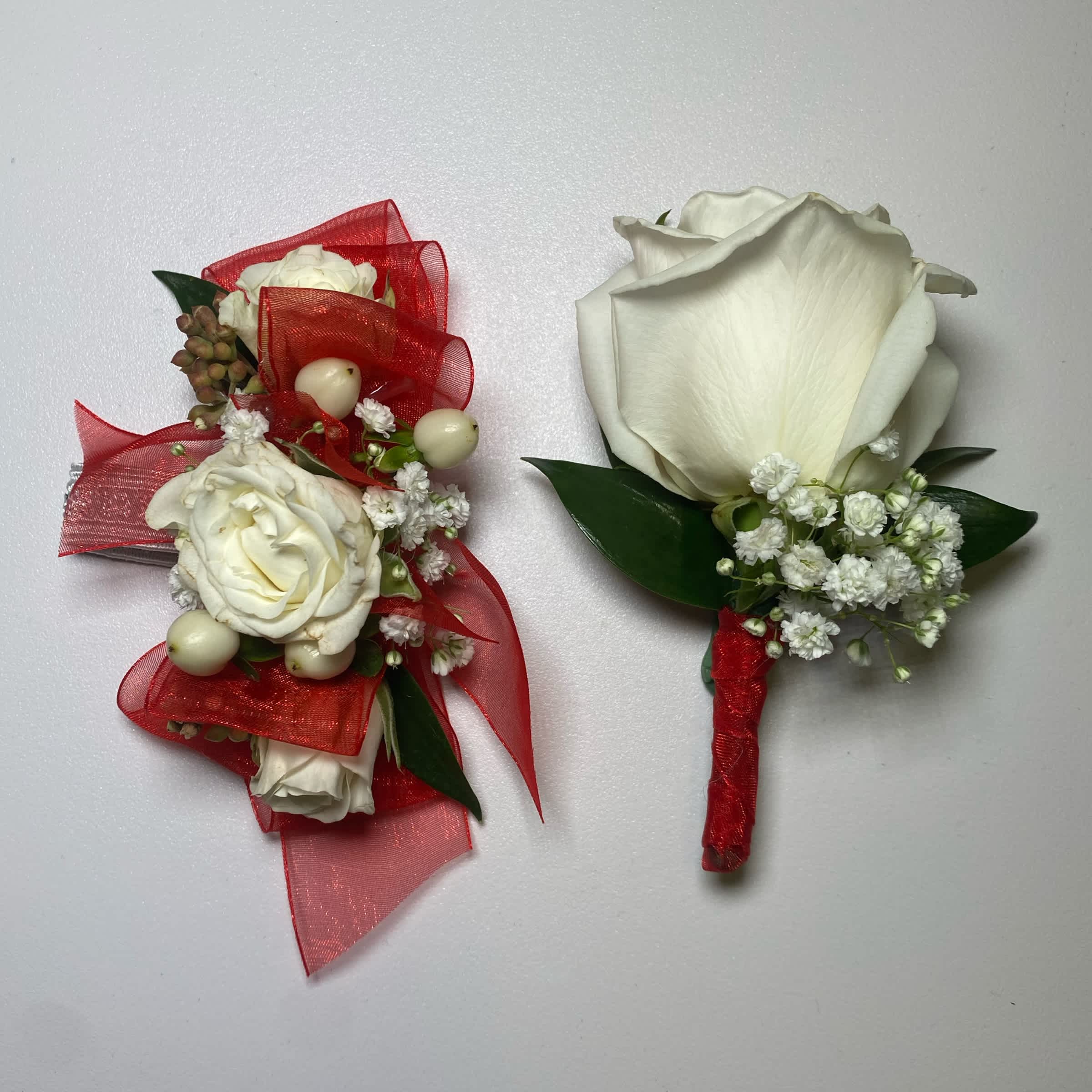 Red Set - Prom/ Wedding - This White Rose Corsage and Boutonniere Includes an Adult Size Elastic Wristband Corsage and Magnetic Boutonniere with Red Chiffon Ribbon. The Corsage Includes White Spray Roses, Hypericum Berries, Gentle Greenery and Seeded Eucalyptus. The Boutonniere includes a White Rose with Babies Breath and Gentle Greenery. Or as Similar as Possible.