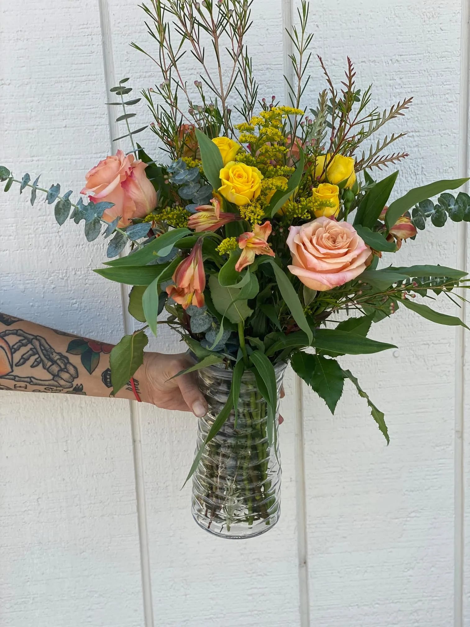Wild & Free Wild & Free - Celebrate her fun wild side with this wild variety of blooms filled with fun textures and color that compliment each other well. Colors are peach roses, yellow spray roses, yellow alstroemerias, baby blue eucalyptus, gravelia