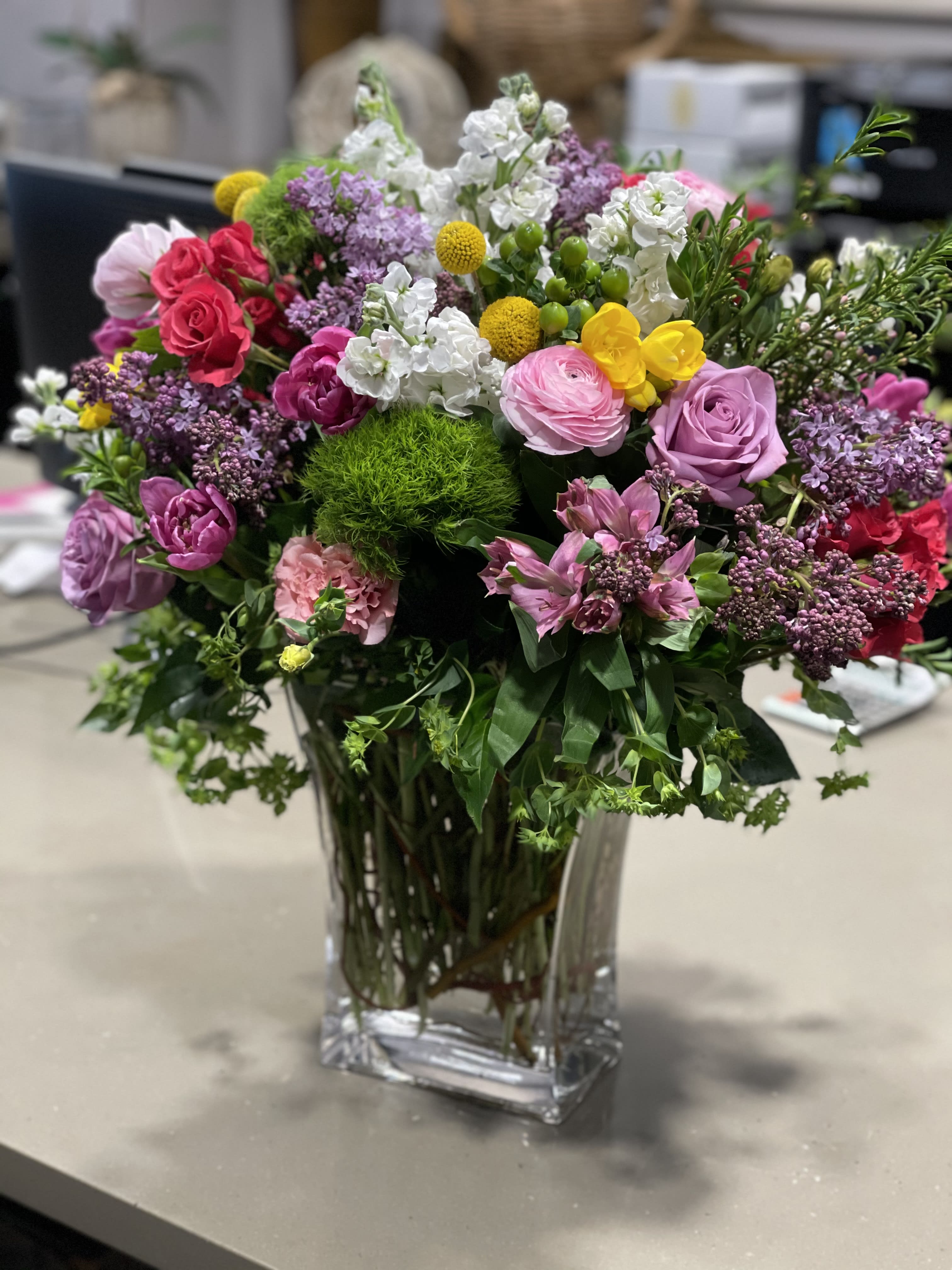 Primavera - Beautiful combinations of Spring flowers like Roses, Tulips, Stock, Ranunculus, Dianthus, freesia and greenery in a tall glass vase. Flowers are subject to change based on availability.  