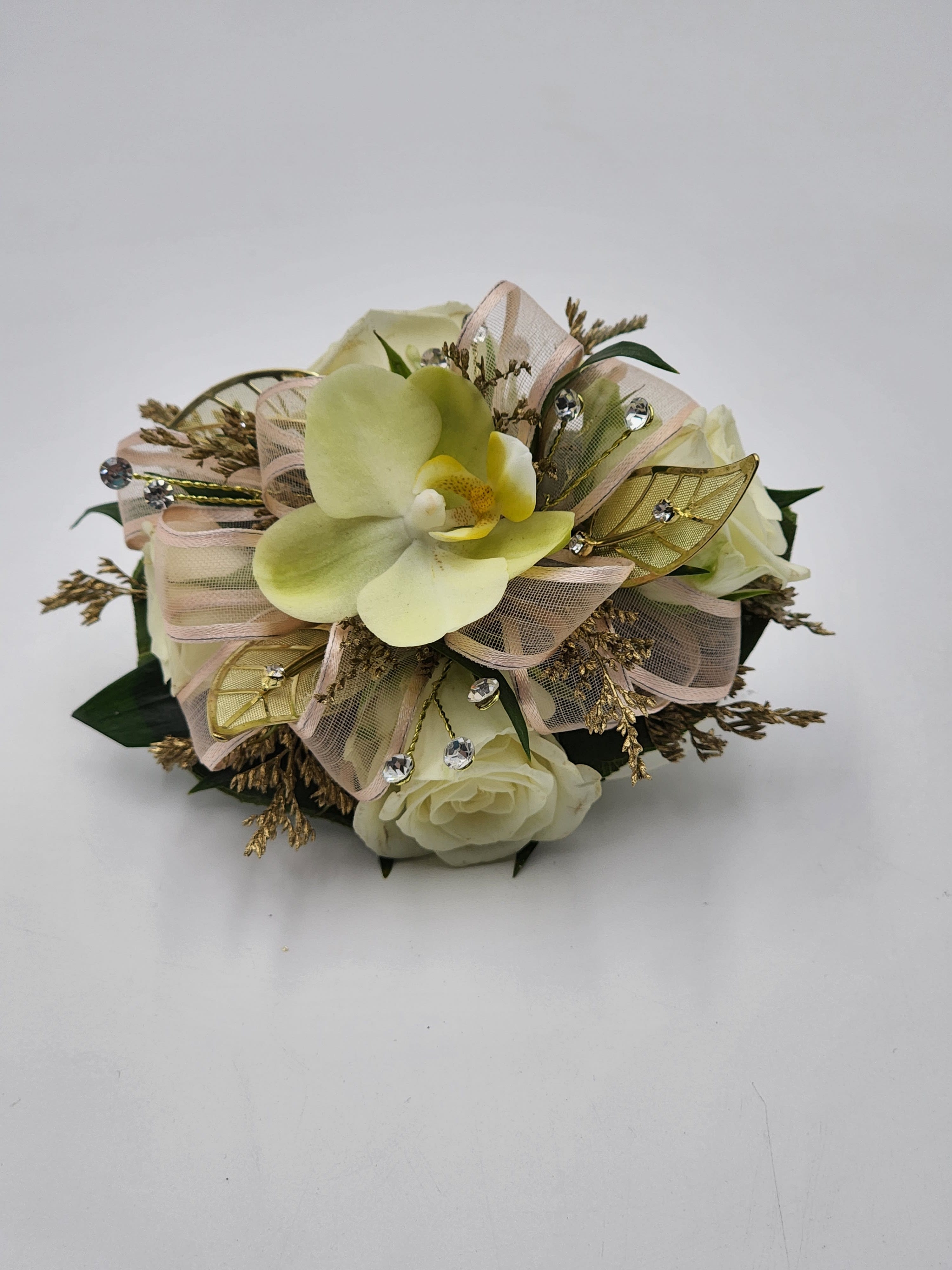 Monarch's Choice Wristlet Monarch's Choice Wristlet - A wrist corsage featuring pale yellow phaleonopsis orchids, white spray roses, clear rhinestones, light pink ribbons and gold leaf accents. Also features a pearl bracelet.
