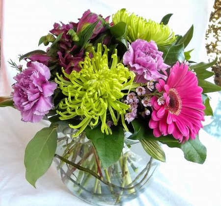 Serenity - A vibrant blend of green, purple and pink blooms arranged in a vase with greenery.