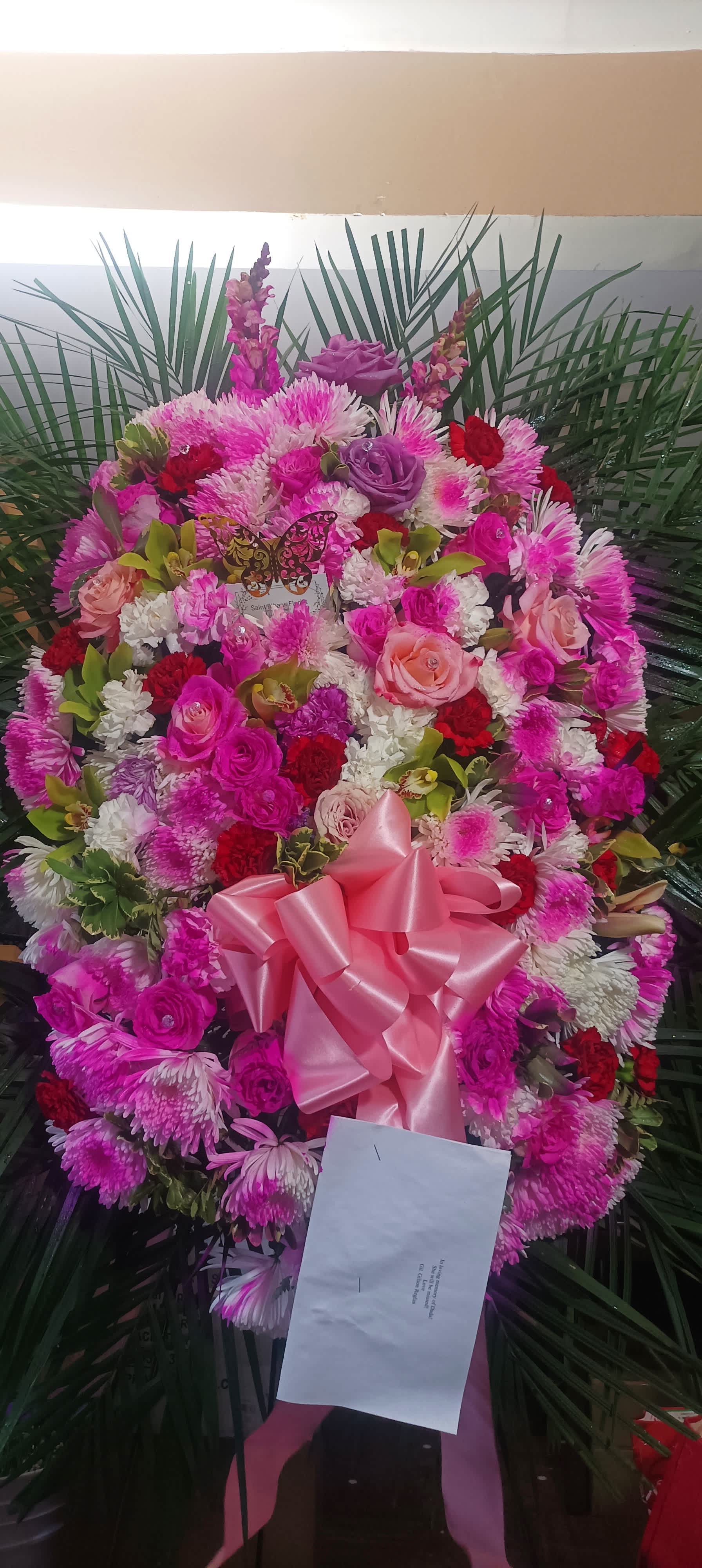 Comforting Pastel Pink Funeral Spray - A beautiful way to send off a female colleague or female co-worker or Boss if family relative or mom. Really beautiful pink.amd white and red flowers with cymbidium orchids, different variety pink roses lilies, gold butterflies, diamonds in the roses. A really beautiful way to send off a loved one.