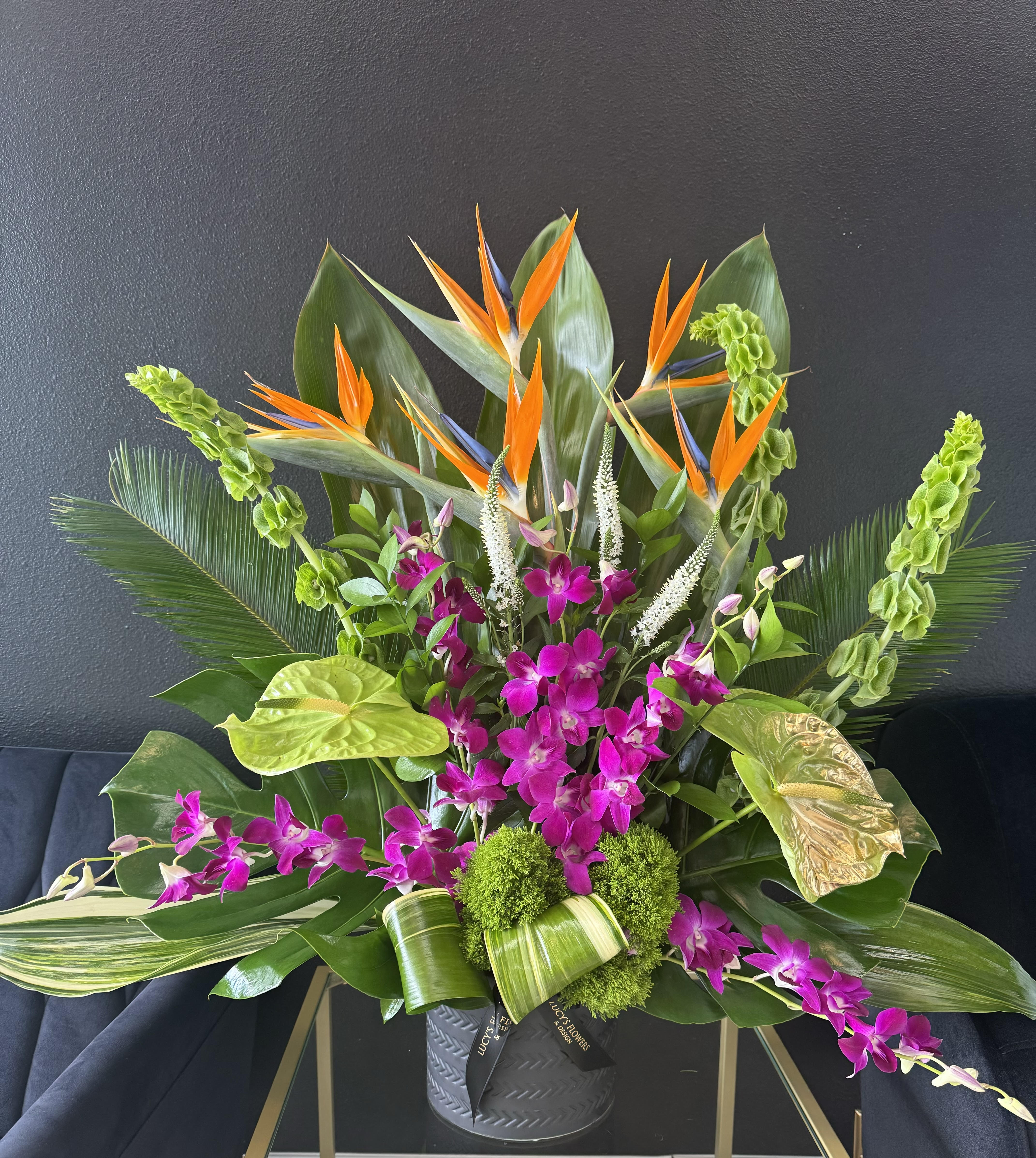 Artistic Mix - Tall, lovely and just right for any occasion! An artistic mix of  tropical flowers such as orchids, birds of paradise, bells of ireland  and anthurium in complementary shades of bright green and purple – arranged in a luxury ceramic  vase – is wonderfully stylish, and will bring pleasure to someone’s day.