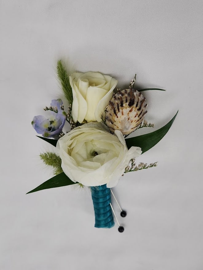 Atlantis Boutonniere Atlantis Boutonniere - Select this Atlantis themed boutonniere featuring ranunculus, bunnytail and belladonna with small sea shells wrapped in blue ribbon. Each boutonniere comes with two metal pins to pin on a jacket lapel or shirt. Exact flowers may vary.