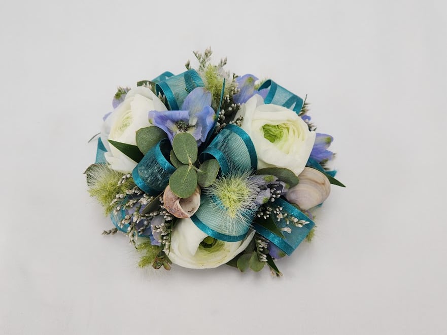 Atlantis Wristlet Atlantis Wristlet - Select this sea themed wristlet corsage with white ranunculus, filler flower, bunnytail, belladonna with a blue ribbon and accents of seashells. This wristlet corsage will come on a simple silver elastic band. Exact flowers may vary.