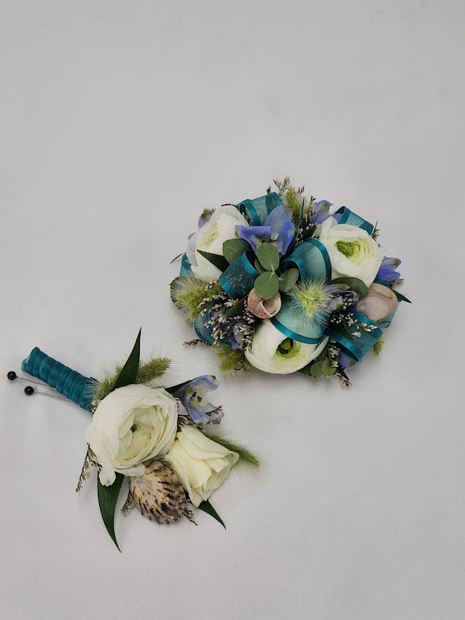 Atlantis Boutonniere and Wristlet Set Atlantis Boutonniere and Wristlet Set - Select this Atlantis themed set featuring ranunculus, bunny tail, misty, bella donna and seashells with blue ribbon. The wristlet will come on a standard grey wristband that is elastic. The boutonniere will come with two black pins to pin on their lapel or shirt.