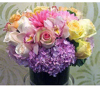 Heavenly Scent - This beautiful soft tone arrangement is made in a low cylinder with a green t-leaf wrapped inside for a clean look. the arrangements contains lavender hydrangeas, soft yellow and peach roses, vendela roses, pink dahlias, and light pink cymbidium blooms.