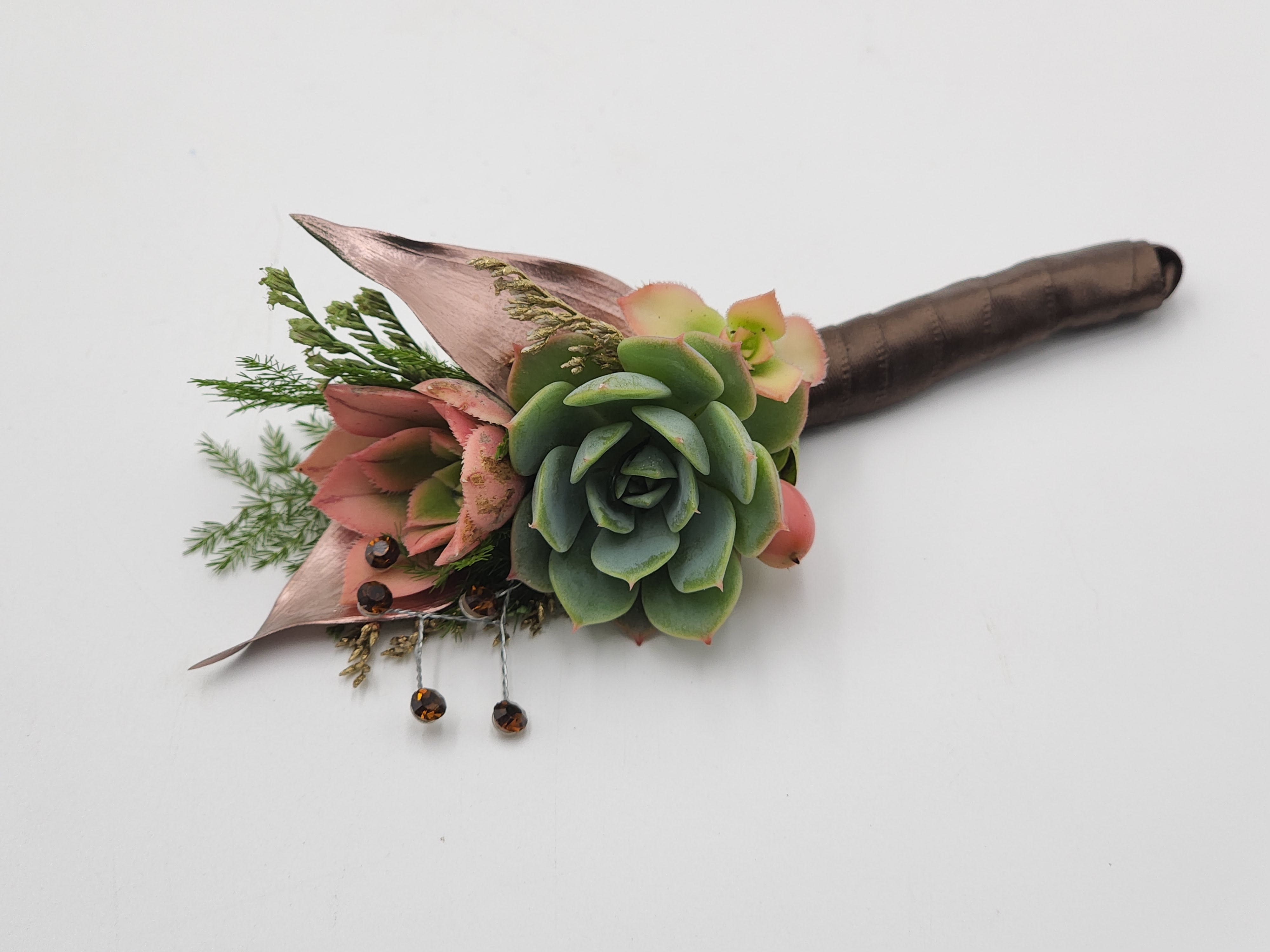 Into the Woods Boutonniere Into the Woods Boutonniere - A boutonniere featuring succulents, chocolate brown ribbon and a rhinestones. Depending on availability of ribbon, may change slightly.