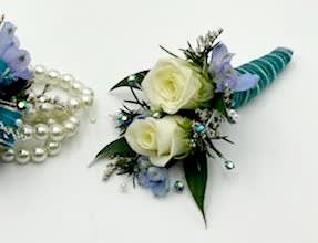 Seaside Secret Boutonniere Seaside Secret Boutonniere - A boutonniere featuring white spray roses, blue belladonna, turquoise ribbon and peacock colored rhinestones. Depending on availability of ribbon, may change slightly.