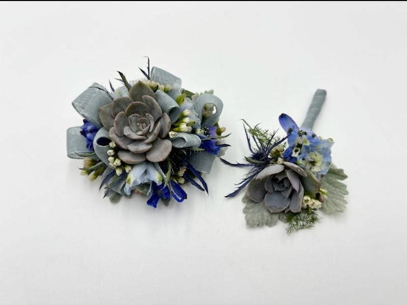 Shades of Blue Boutonniere And Wristlet Set Shades of Blue Boutonniere And Wristlet Set - A boutonniere and wrist corsage set featuring blue toned succulents, belladonna and blue-gray ribbon. Depending on availability of ribbon, may change slightly.