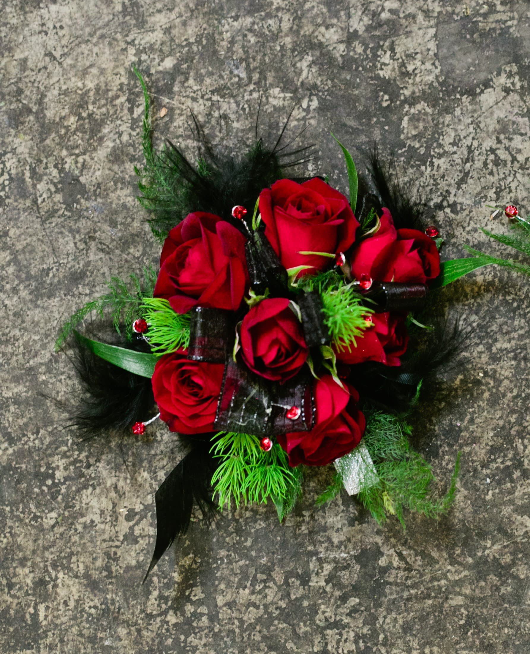 Witchcraft Wristlet - Select this bewitching corsage consisting of red spray roses with black feathers and red rhinestones. ALL PROM FLOWERS ARE AVAILABLE IN COLORS PICTURED OR A CUSTOM SELECTION. CHOOSE YOUR FLOWER COLORS, RIBBON COLOR AND ANY ADD ONS. FOR QUESTIONS CALL A FRIENDLY SALES REPRESENTATIVE AT STRELITZIA FLOWER CO.