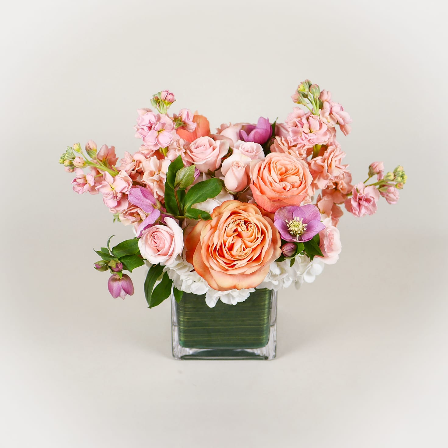 Princess Peach - This bright arrangement boasts white hydrangeas, peach roses, fragrant peach stock, and hellebores in a 5&quot; leaf-lined glass square. Full and lush, it's the perfect captivating gift and one of our most popular sellers!