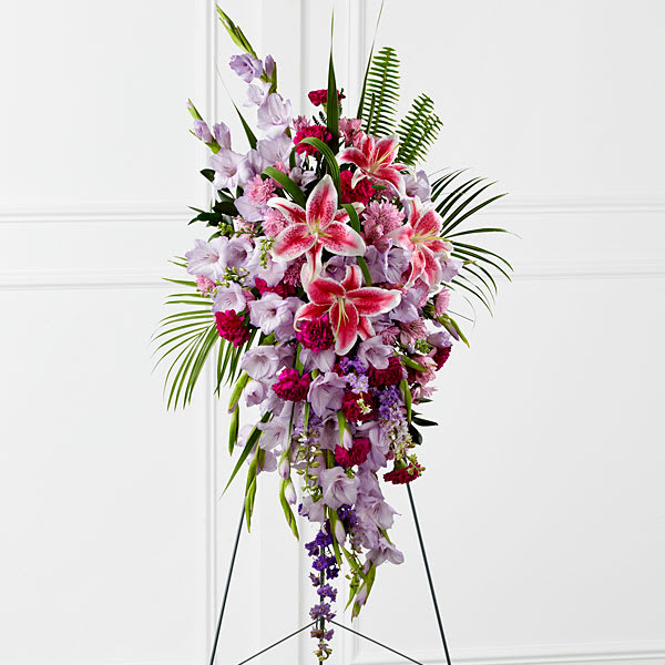 Tender Touch Standing Spray -  Tender Touch™ Standing Spray creates an elegant display of beauty and color to enhance their final tribute. Lavender gladiolus Stargazer lilies fuchsia carnations purple larkspur lavender Peruvian lilies lavender chrysanthemums sword fern fronds emerald palm fronds and other assorted greens are gorgeously arranged to create a sophisticated standing spray. Displayed on a wire easel this arrangement will add to the sophistication of their service with each fragrant bloom.