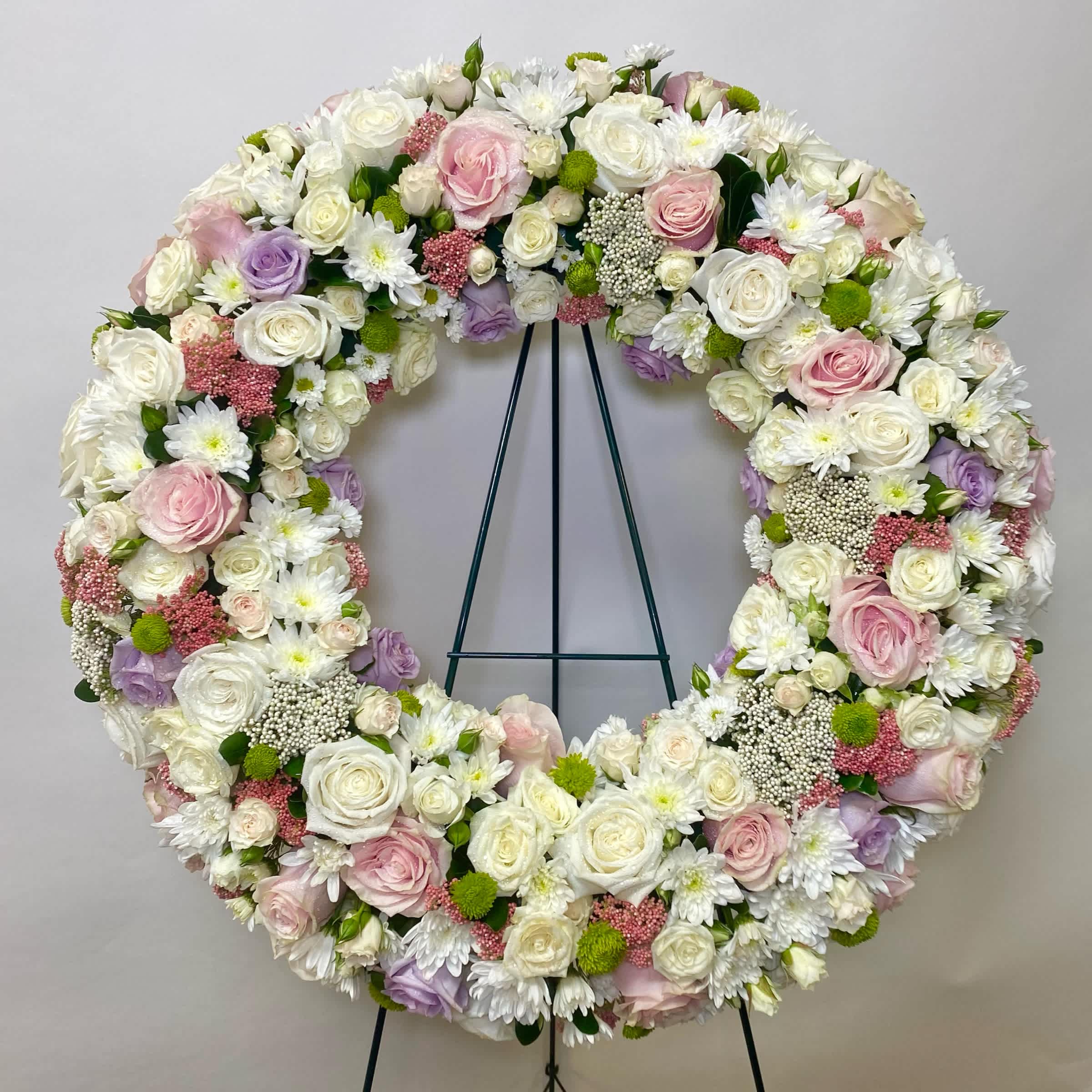 Garden Of Light Wreath - This Wreath Includes White Roses, Light Pink Roses, Lavender Roses, White Spary Roses, White Cushion Mums, Green Button Mums, and White and Pink Rice Flower Or White and Pink Wax Flower. Or as Similar as Possible. 