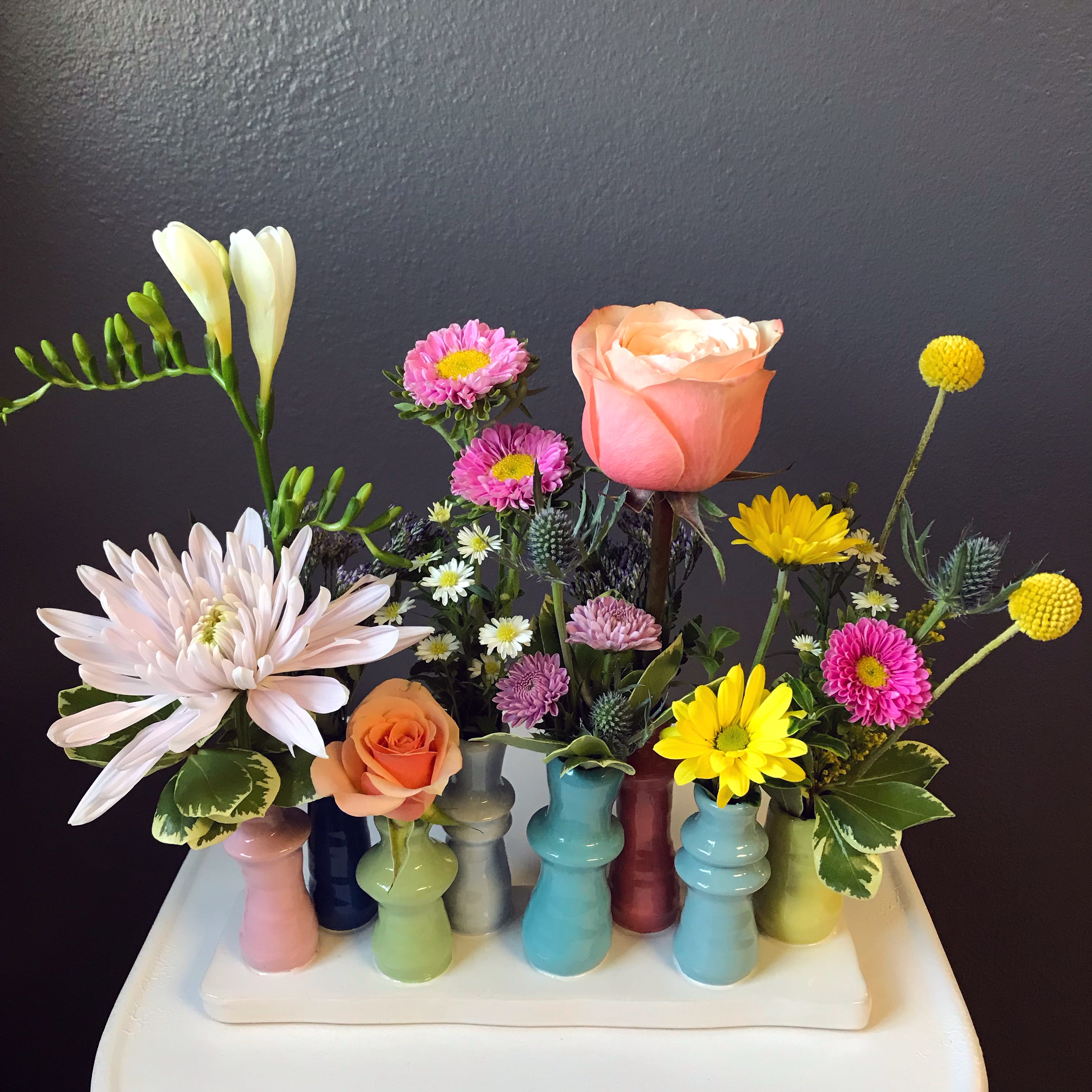 Molly Marie - A unique platform of colorful ceramic bud vases filled with cheery blooms. This fun arrangement is sure to bring a smile, and also makes for a great keepsake. Approximately 10&quot; wide x 12&quot; tall. 