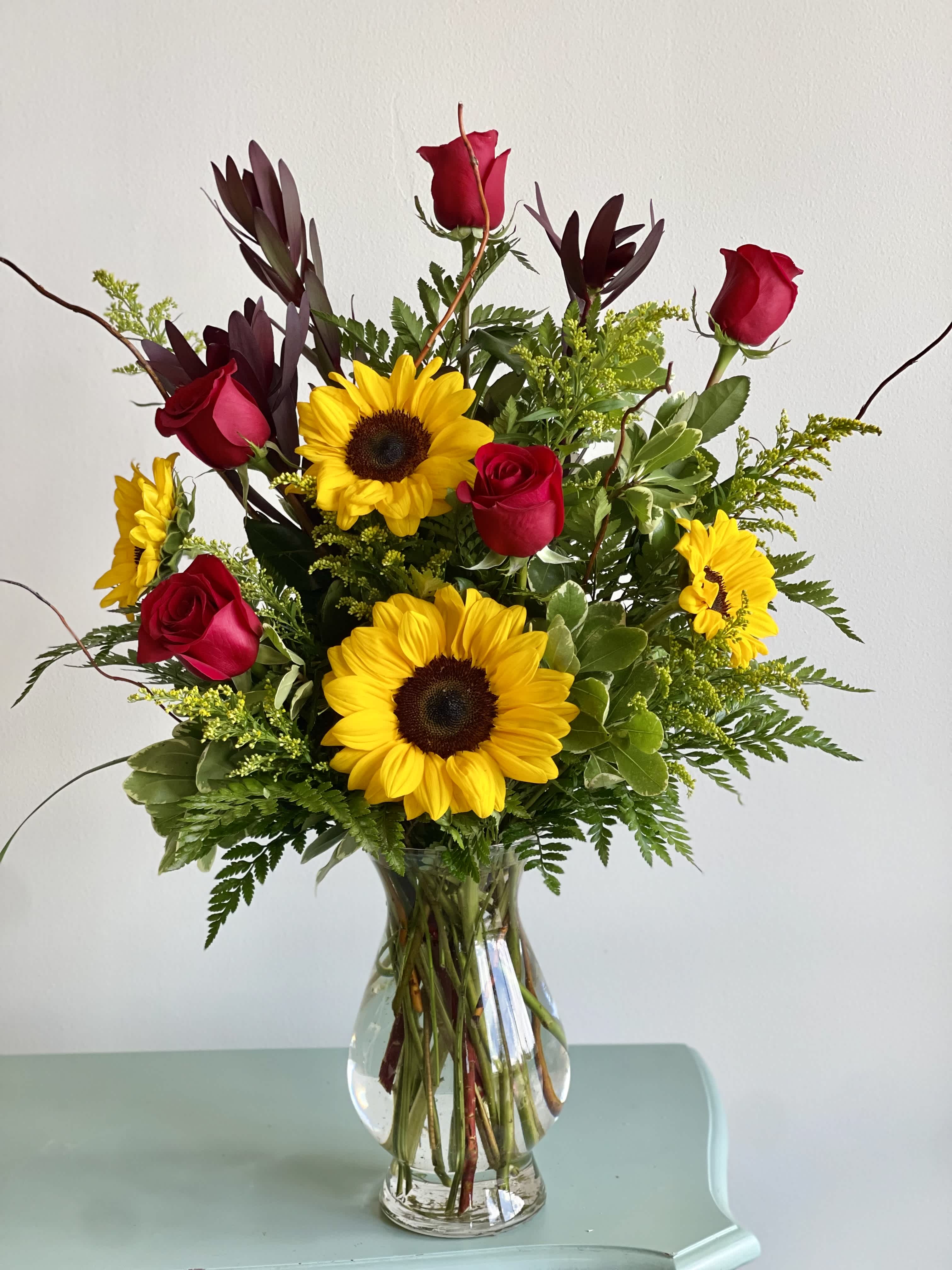 Sunsation - A sensational arrangement of buttery sunflowers, scarlet roses accented with solidago and lush foliage will bring bright smiles from the recipient.