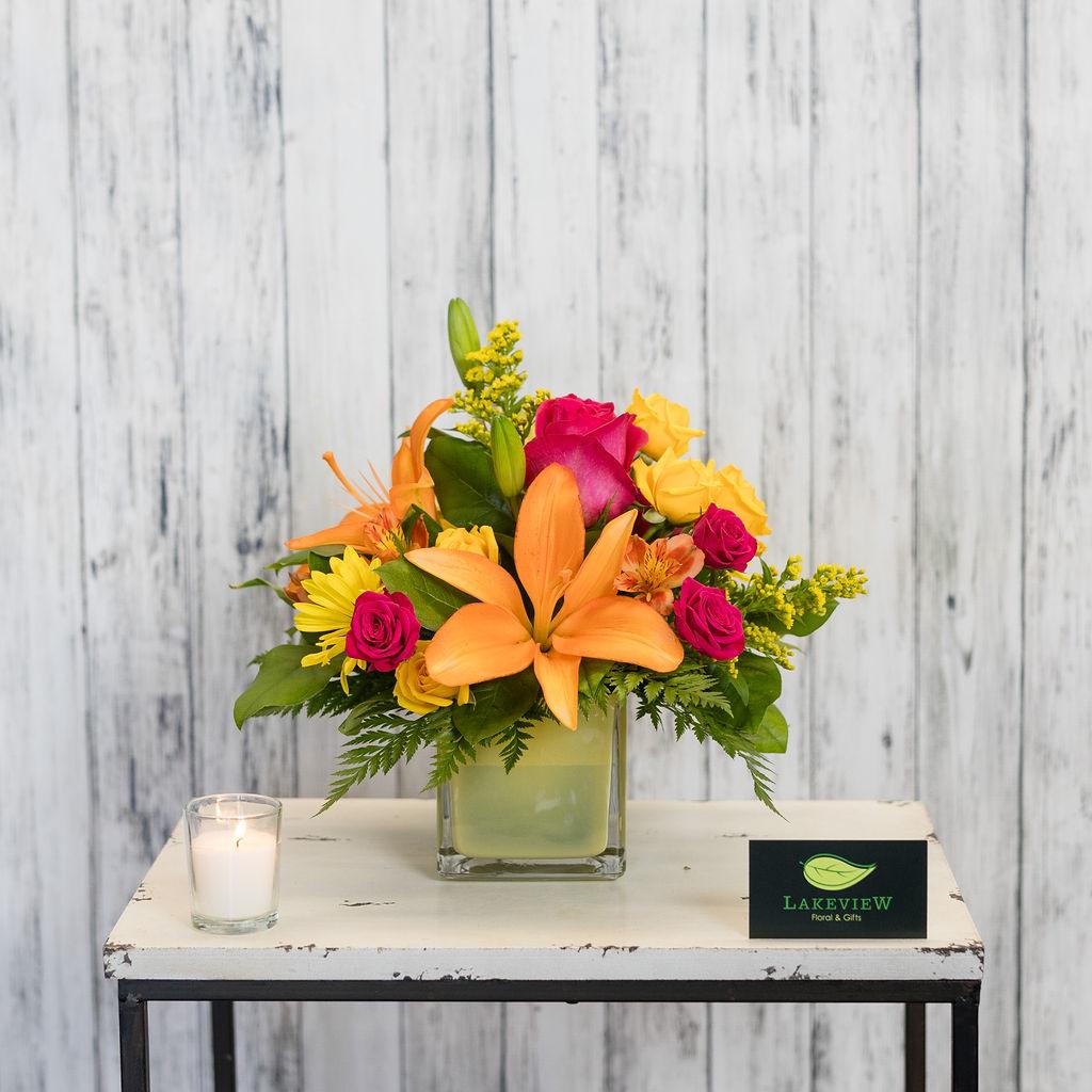 Tangerine - Bright and cheery uplifting blooms in a fun yellow glass cube are sure to brighten anyone's day! This arrangement  includes Asiatic lilies, spray roses, alstroemeria, daisies, and solidago.   Arrangement size is approximately 12&quot; H X 12&quot; W