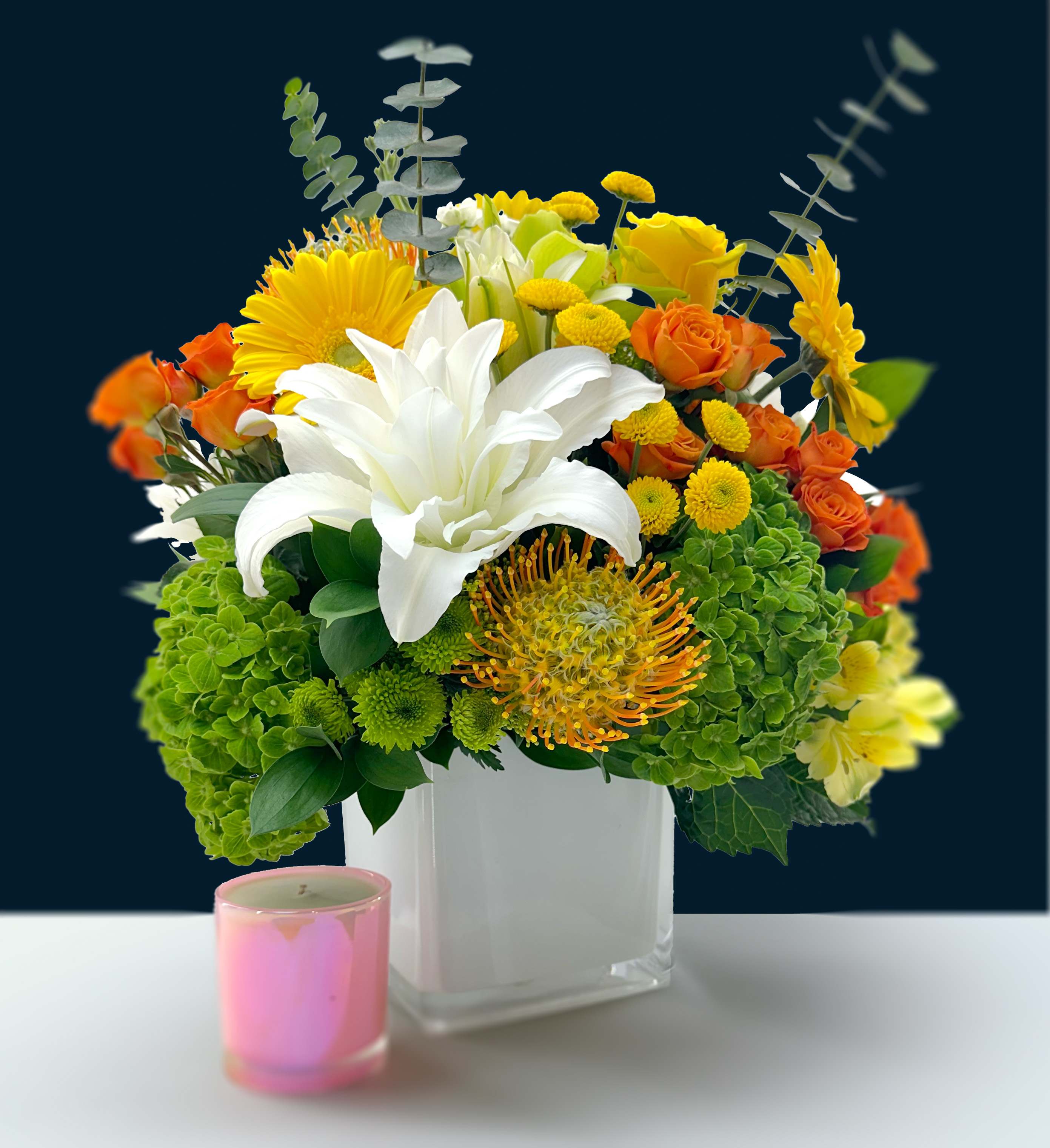 Citrus Splash  - Bring some sunshine indoors with the vibrant hues of our “Citrus Splash”. This bouquet is composed of pincushion protea, cymbidium orchids, gerbera, daisies, lilies, spray roses, and more seasonal blooms. It will arrive in a 6”(15.24cm) cube vase.  *Candle depicted is for scale, sold separately. *