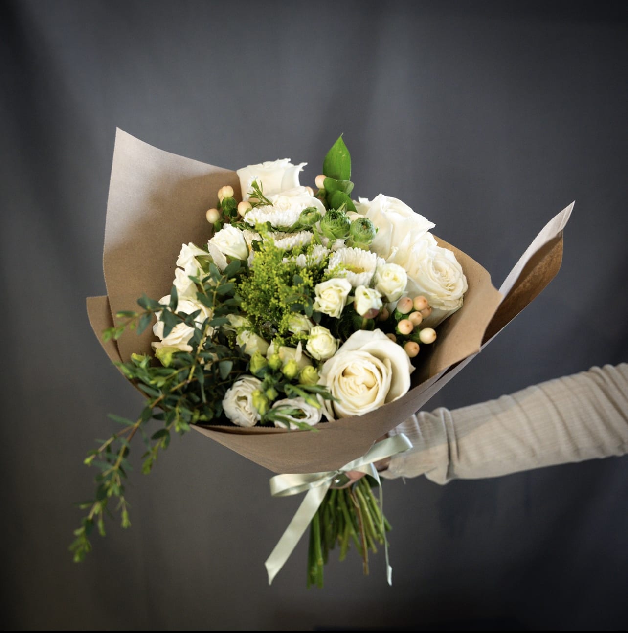 Bouquet Bianco  - Fresh and elegant hand-tied white bouquet wrapped in rustic butcher paper, featuring a stunning arrangement of white roses, delicate spray roses, and other fresh flowers. Perfect for weddings, anniversaries, or any special occasion. Our expertly crafted bouquet is sure to impress with its timeless beauty and natural charm. Order now for quick delivery!