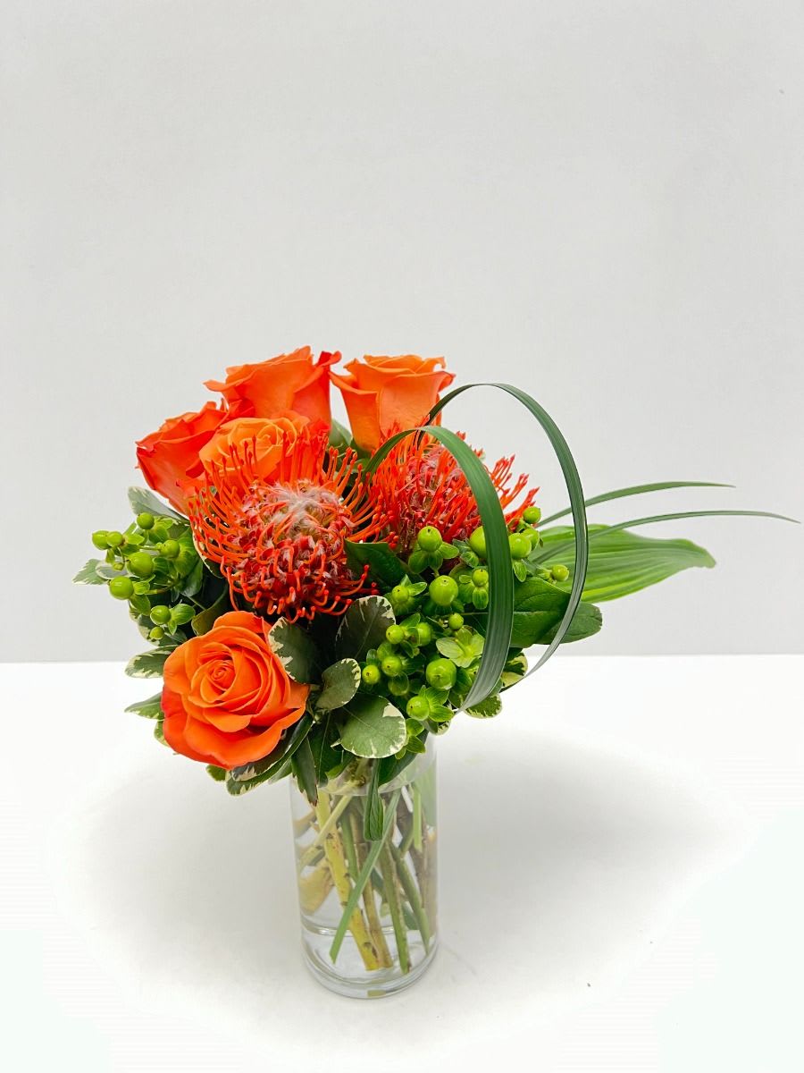 SFD20186 - Beat The Heat - SFD20186 - Beat The Heat A bright and modern combination of pin cushion proteas and orange roses with hypericum berries and greenery perfect as a compliment on a side table or desk.
