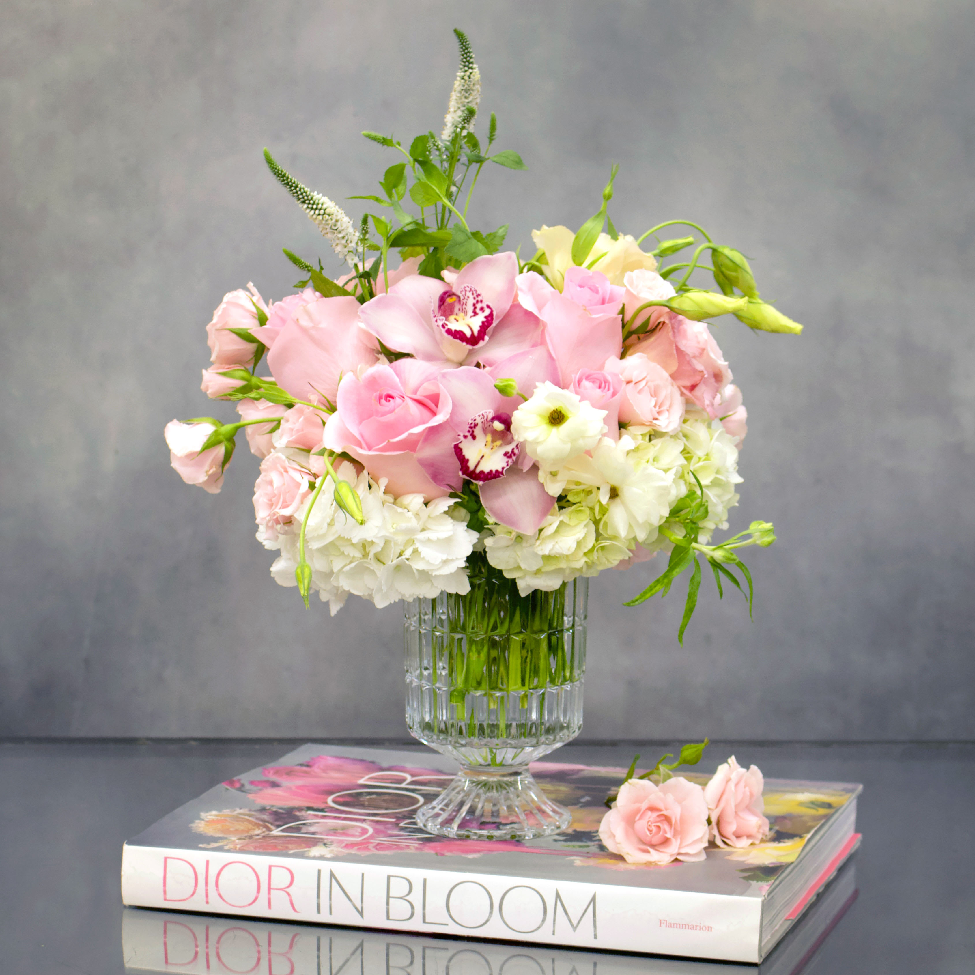 Pink Delight Short - Sherman Oaks Florist - Admire the beauty of a delicate arrangement featuring soft pink roses, luxurious orchids, and pristine whites in a charming pedestal vase. Standing at approximately 10 inches tall and 8 inches wide, this floral masterpiece adds a touch of sophistication and natural allure to any space.