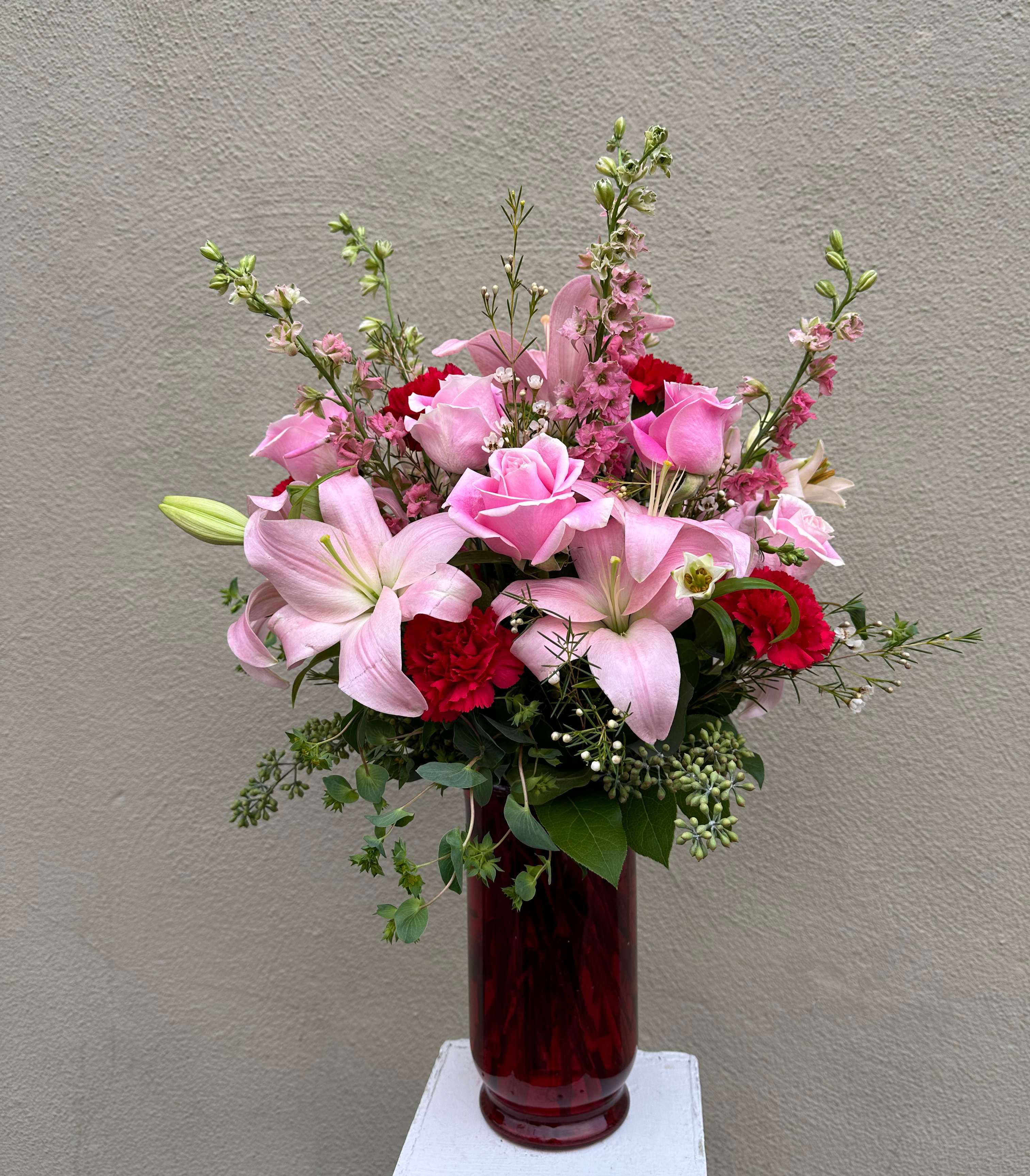 Pink Expression - This truly original arrangement of pink roses, lilies, carnations, larkspur, waxflower and more will leave her smiling brighter than the vase it arrives in! We think it's a brilliant gift idea for birthdays, anniversaries or Valentine's Day you want to put that special someone in the spotlight. Luxurious arrangement of gorgeous pink roses, lilies, carnations, Larkspur and waxflower, accented with seeded eucalyptus, bupleurum and salal Artistically designed by our expert florists.; red glass bell vase measures 10&quot;H