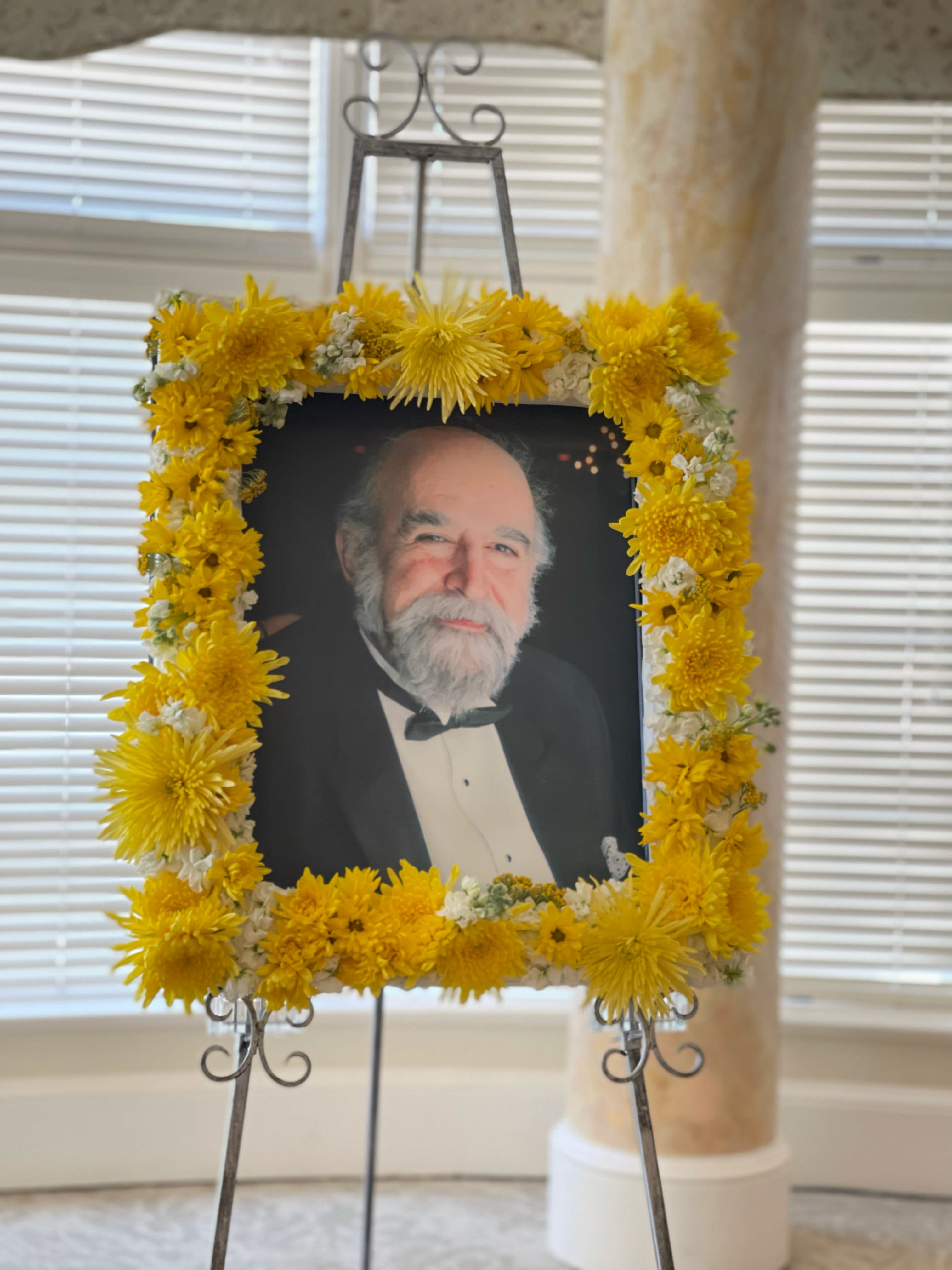 Sunshine + Smiles Memorial Photo Wreath - You provide the photo, we provide the beautiful flowers.   Filled with bright and happy daisies, mums, yarrow, stocks.  Approx size is 2ft wide, 1 ft tall, comes with 6ft stand