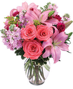 Supremely Lovely Supremely Lovely - 6.25" clear ginger vase foliage: leather leaf, variegated pittosporum 5 stems lavender stock 3 stems burgundy mini carnations 2 stems medium pink lilies 3 coral roses 3 stems solidago