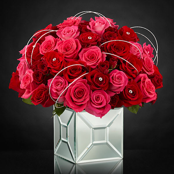 The Blushing Extravagance Luxury Bouquet - Designed to capture the heart this bouquet goes above and beyond to create a space where modern style and love’s every wish unite. Hot pink roses red roses and red spray roses are arranged to perfection and embellished with sparkling stone accents at the center of select blooms as well as silver wires to create a fascinating looping effect taking the average rose bouquet to a new level of sophistication. Tying everything together is the modern mirrored vase that brings light and love to this unique design.